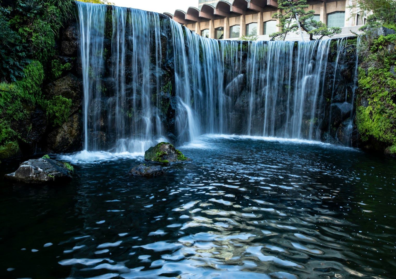 美麗的瀑布場景流入寧靜的水池背景有建築物