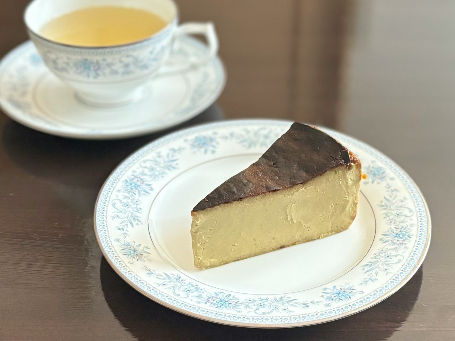 裝飾盤上的一片起司蛋糕，背景中有一個茶杯