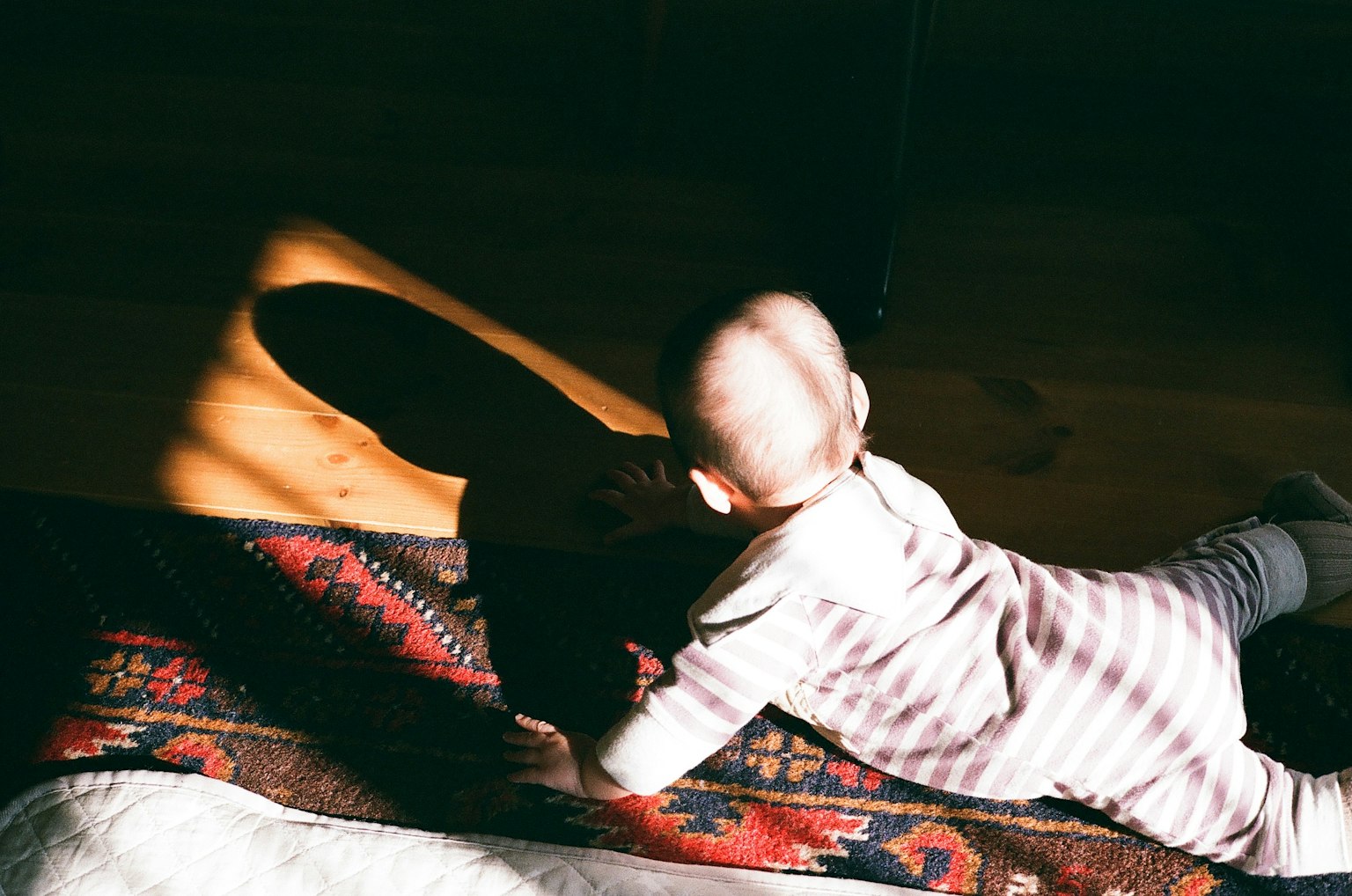 Ein Baby krabbelt auf einem Teppich mit Sonnenlicht, das einen Schatten wirft