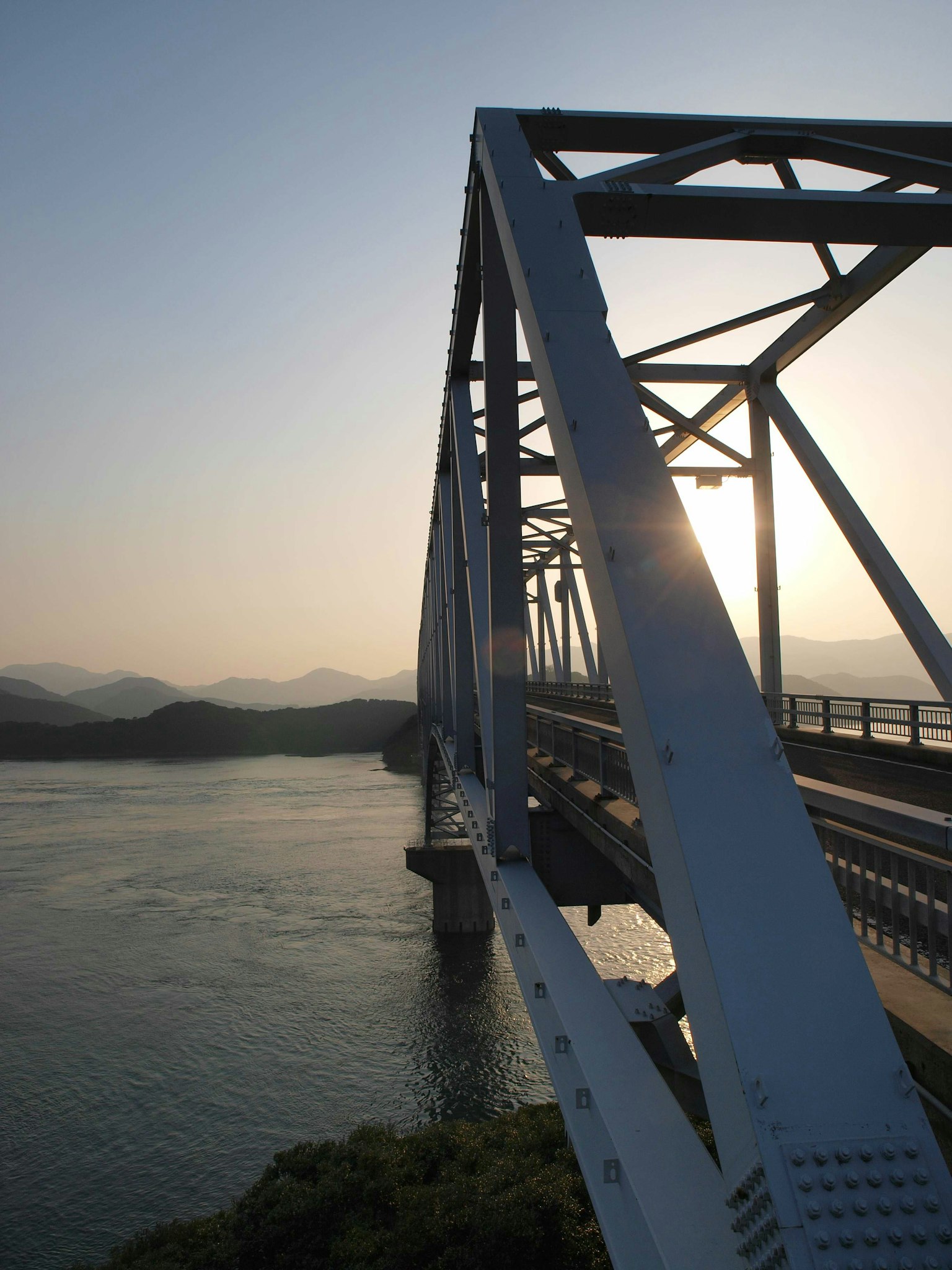 Un ponte in acciaio bianco che attraversa un fiume con un tramonto sullo sfondo