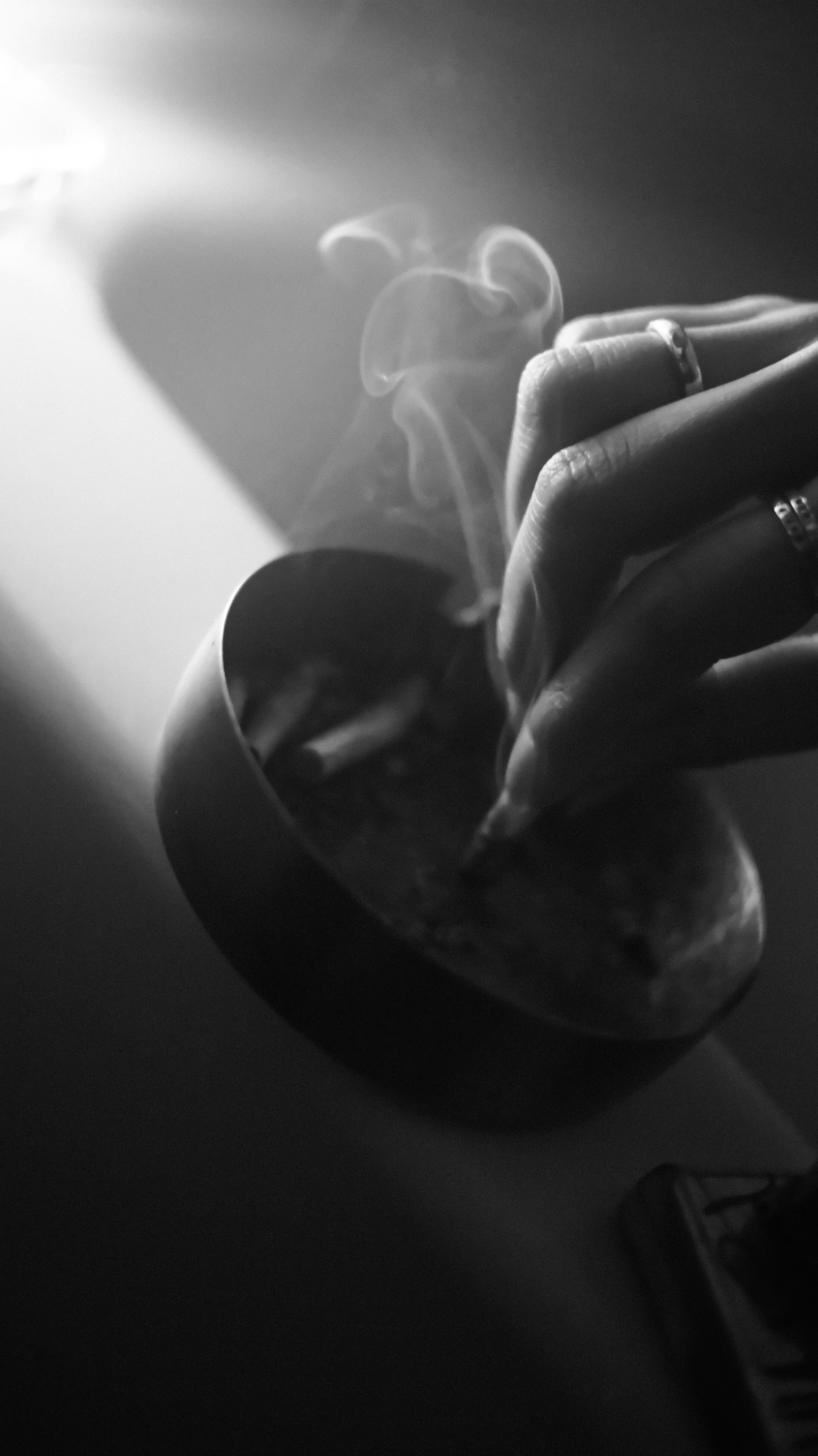 手が灰皿から煙草を取り出すモノクロ写真 煙が漂う光の中で