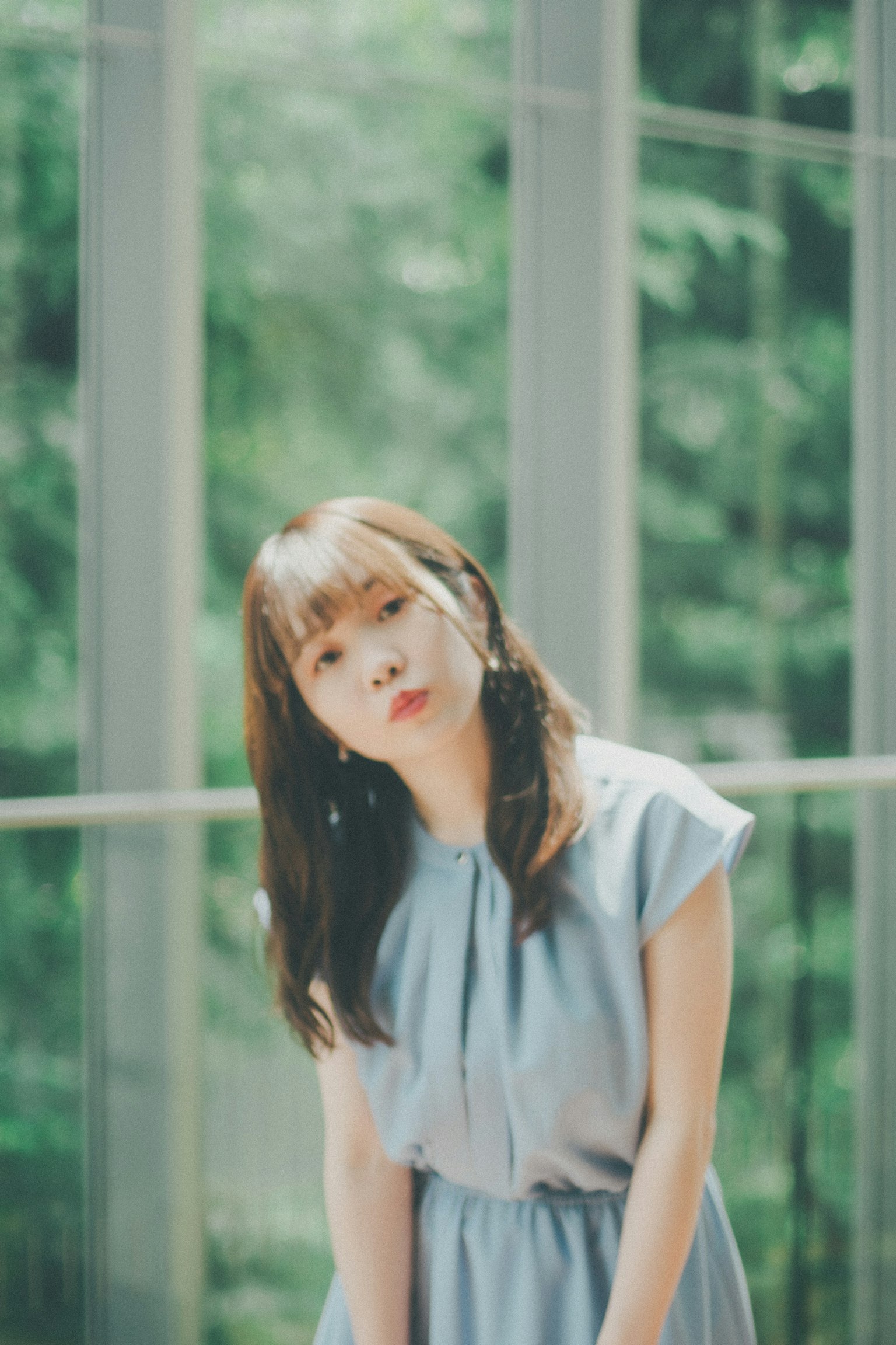창 앞에서 포즈를 취하는 여성, 파란 드레스, 자연광 속 부드러운 표정