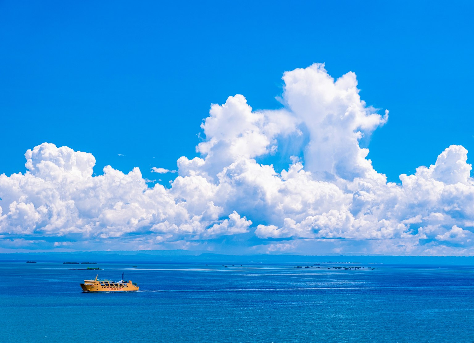 青い海と白い雲の下を航行する黄色い船