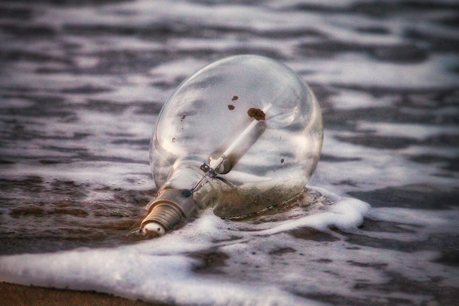 Un fragmento de bombilla transparente descansando en la orilla con olas