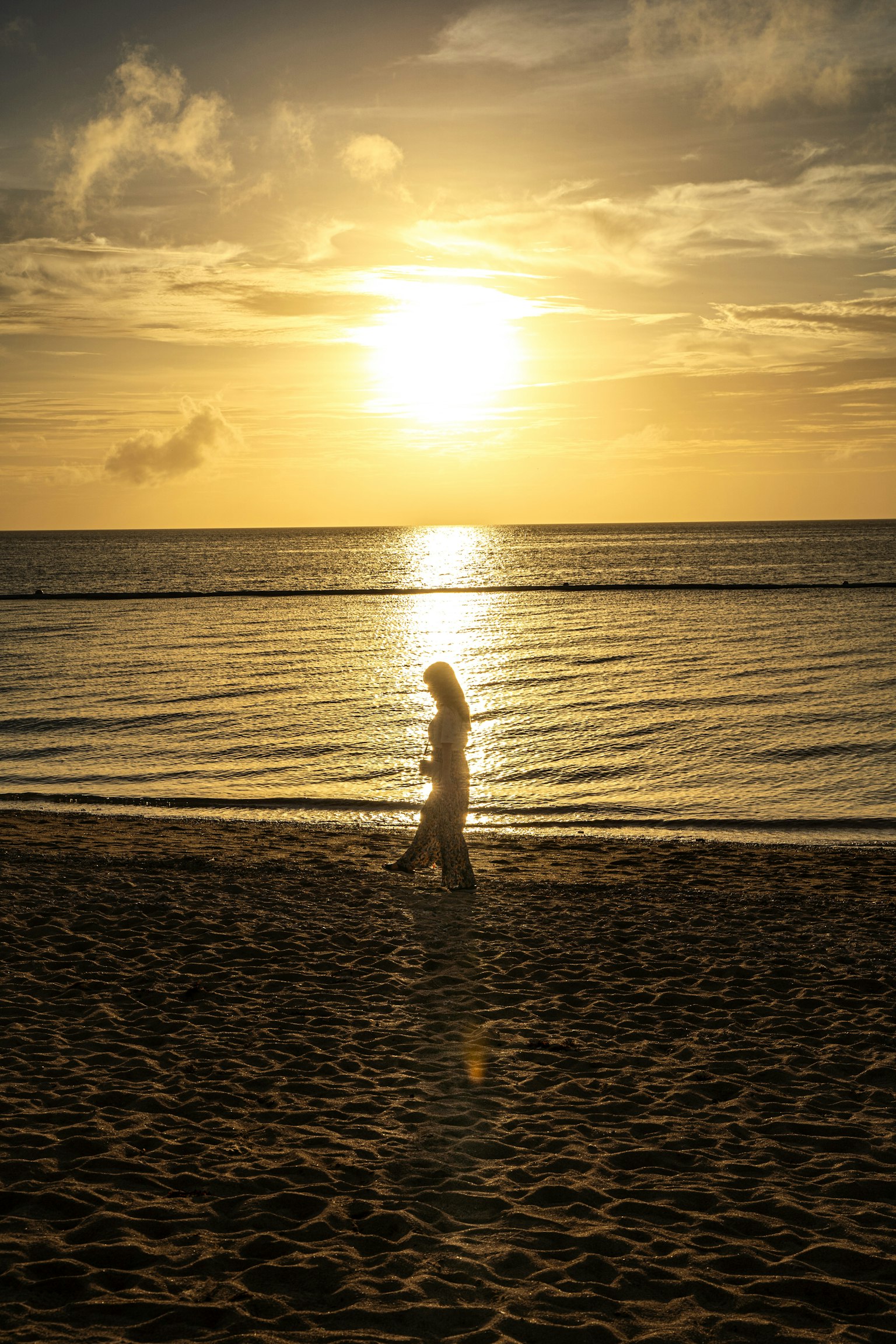 Bóng dáng của một người phụ nữ đi dạo trên bãi biển lúc hoàng hôn