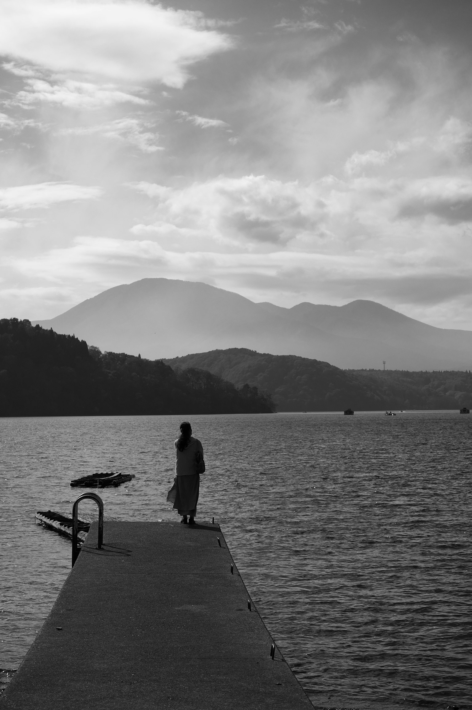 คนยืนอยู่บนท่าเรือข้างทะเลสาบพร้อมภูเขาในพื้นหลัง