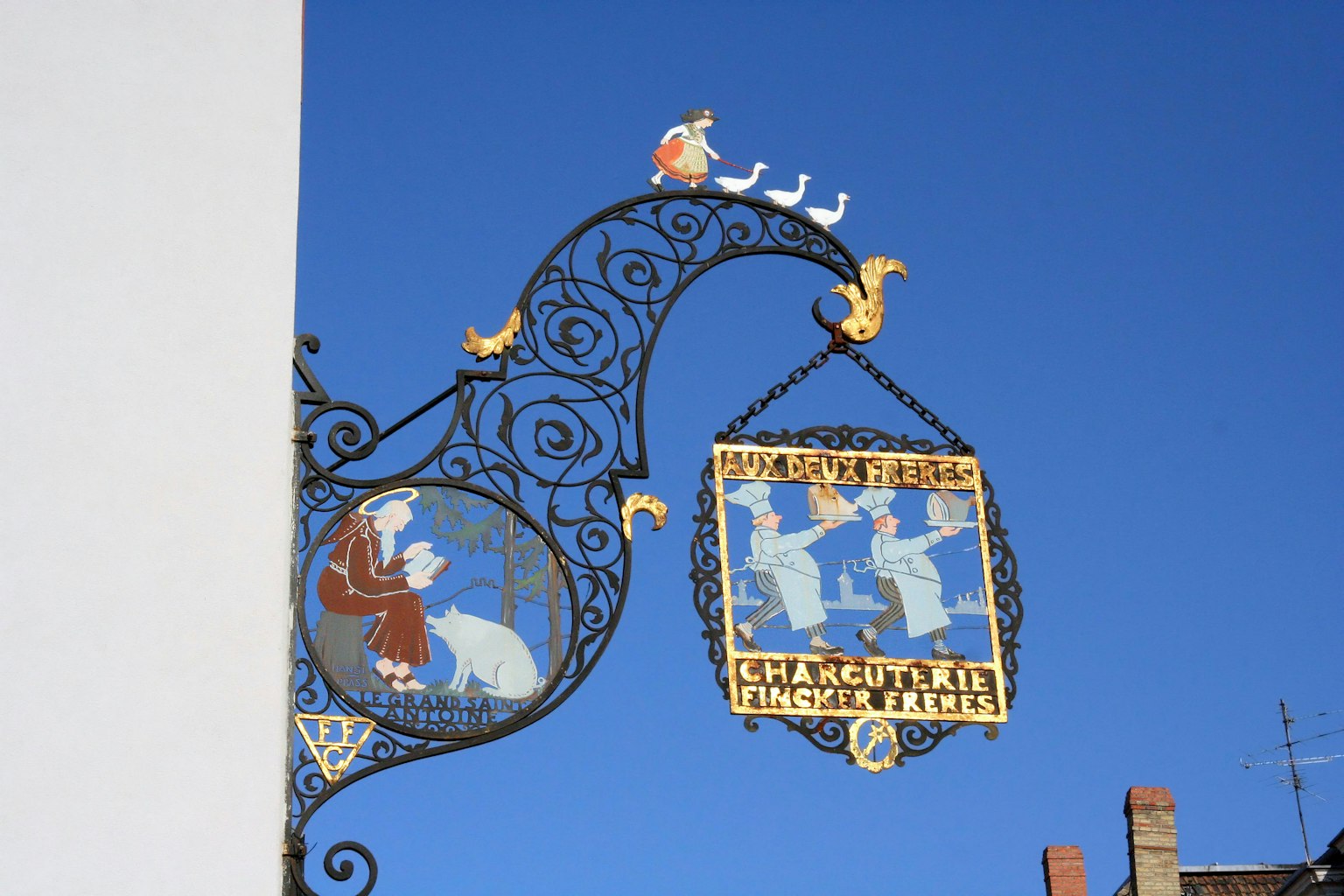 Cartel de hierro decorativo con figuras bajo un cielo azul