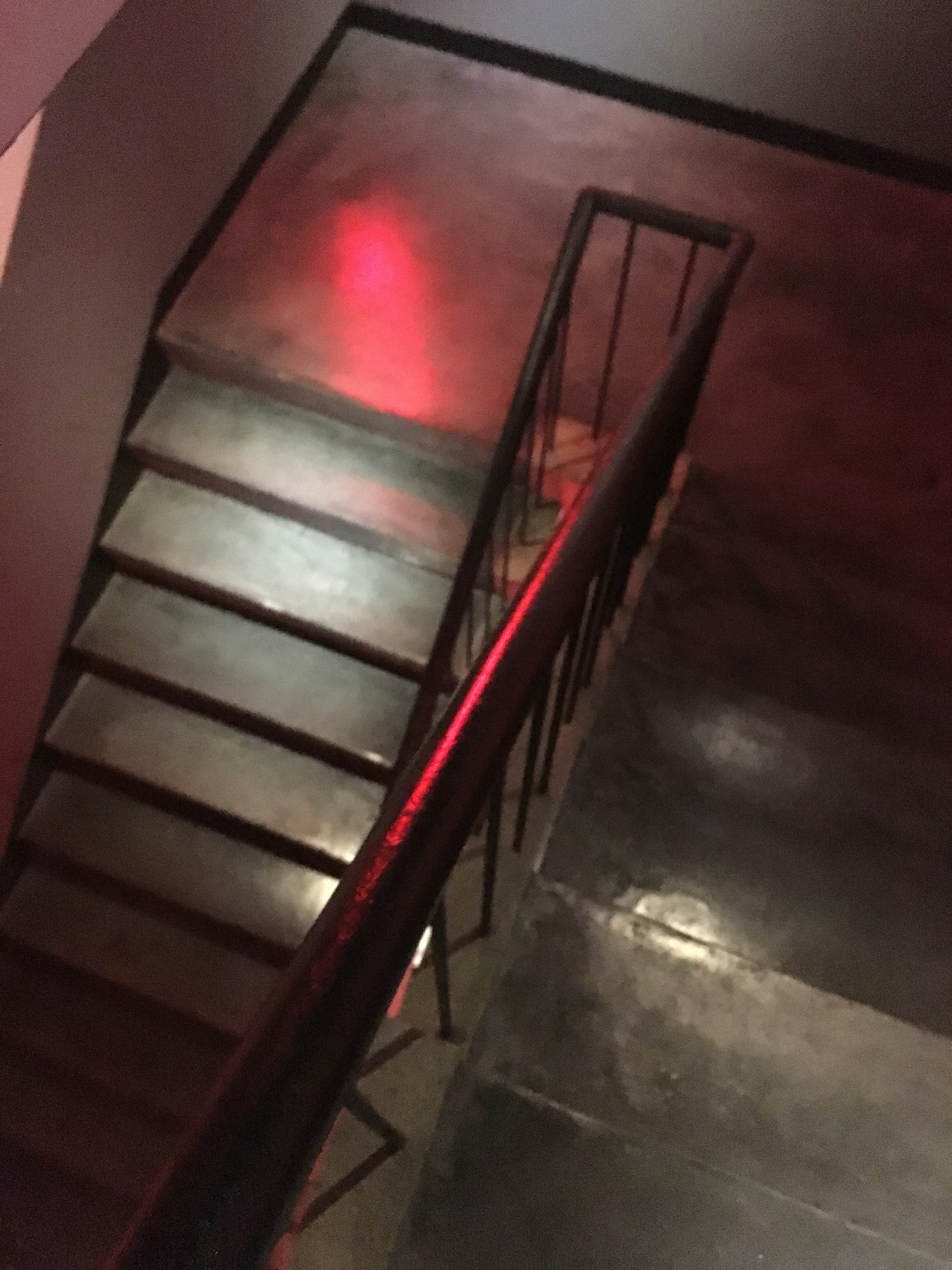 Vista desde arriba de una escalera con barandilla metálica y un reflejo de luz roja en el suelo