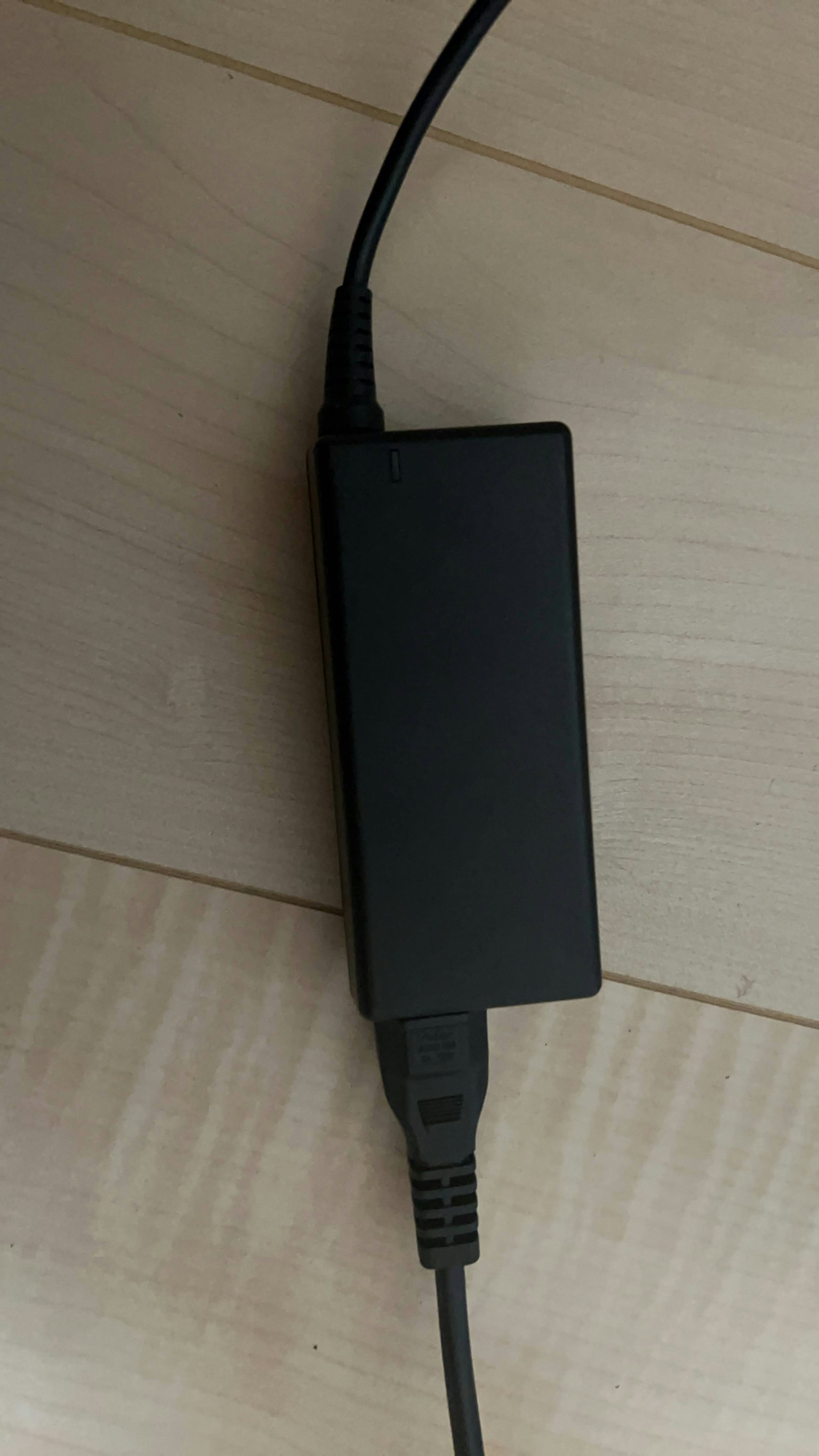 Pengisi daya laptop hitam yang terletak di lantai kayu