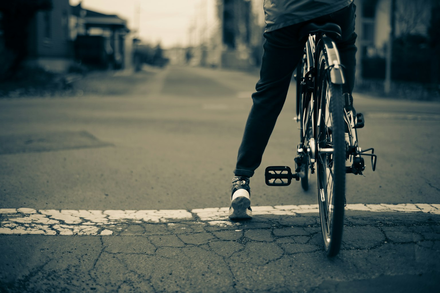 Une personne se tenant avec un vélo à un passage piéton blanc sur une route fissurée