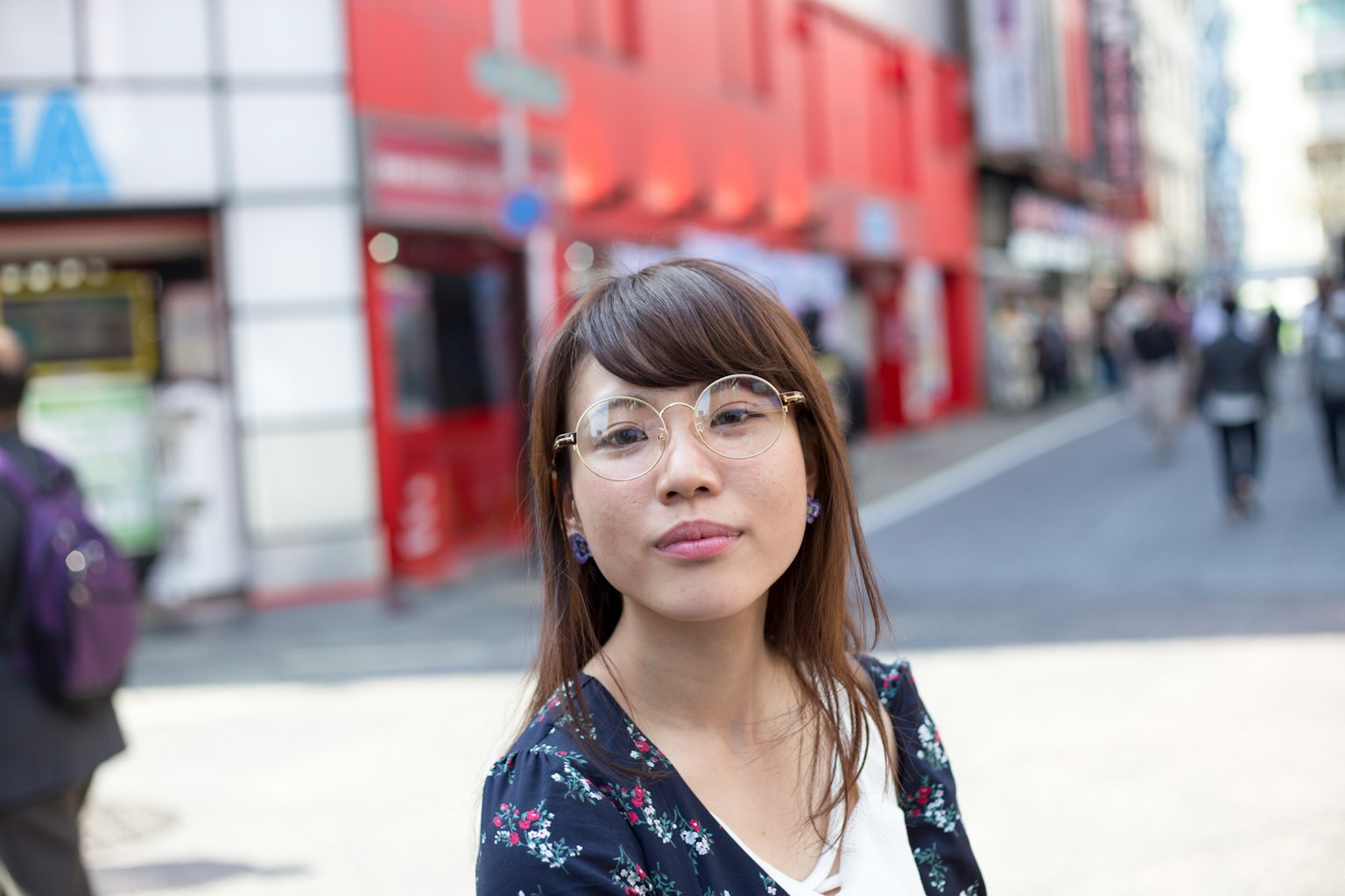 Une femme portant des lunettes dans un cadre urbain avec des bâtiments rouges en arrière-plan