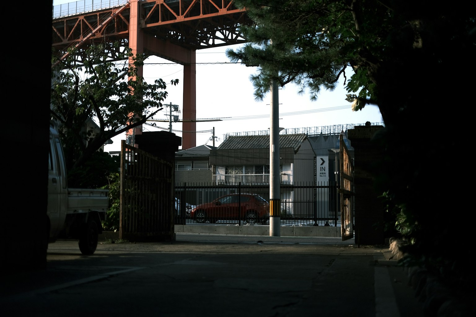Blick auf ein Wohngebiet und ein rotes Auto durch ein Tor unter einer Eisenbahnbrücke