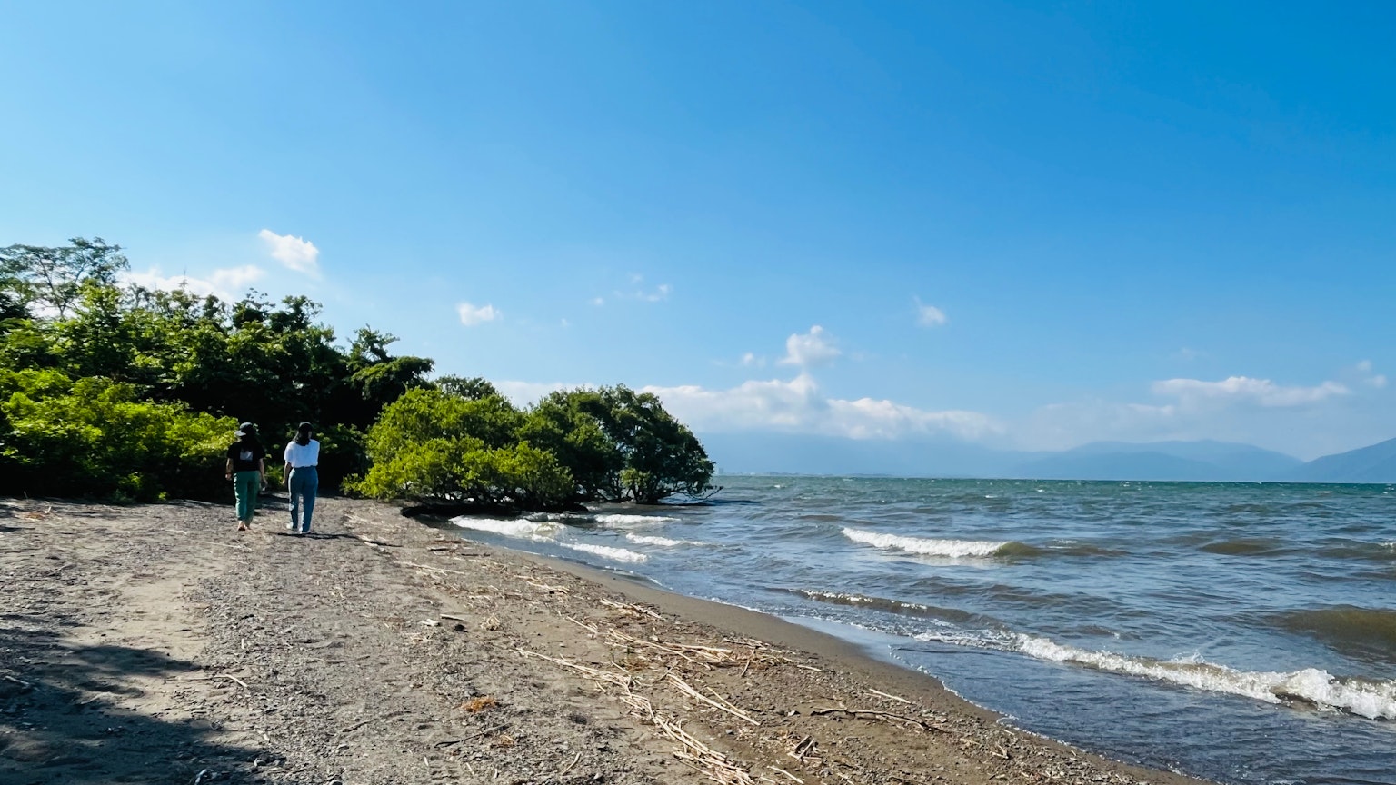 Des personnes se promenant le long d'une plage de lac sous un ciel bleu et des vagues