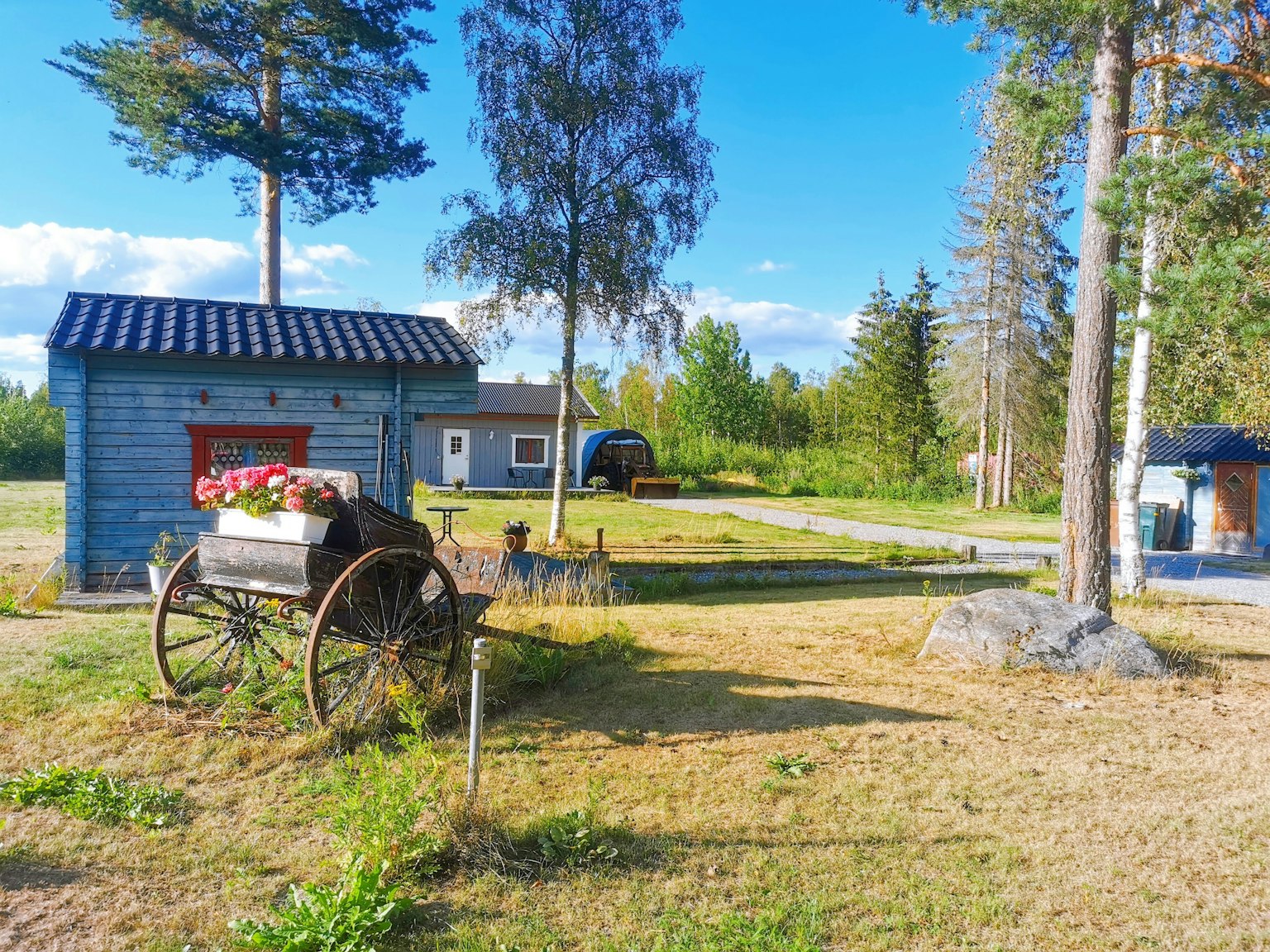 Landscape featuring a blue shed and an old cart under a clear sky