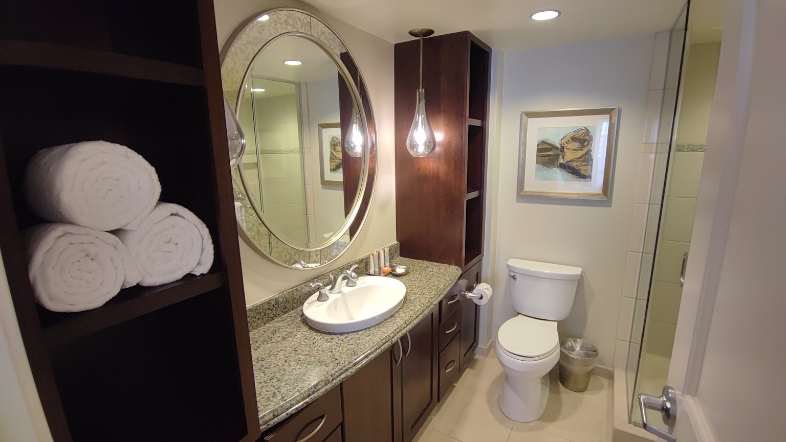 Interno di un bagno moderno con specchio rotondo, lavabo, armadietto in legno, asciugamani bianchi, opera d'arte