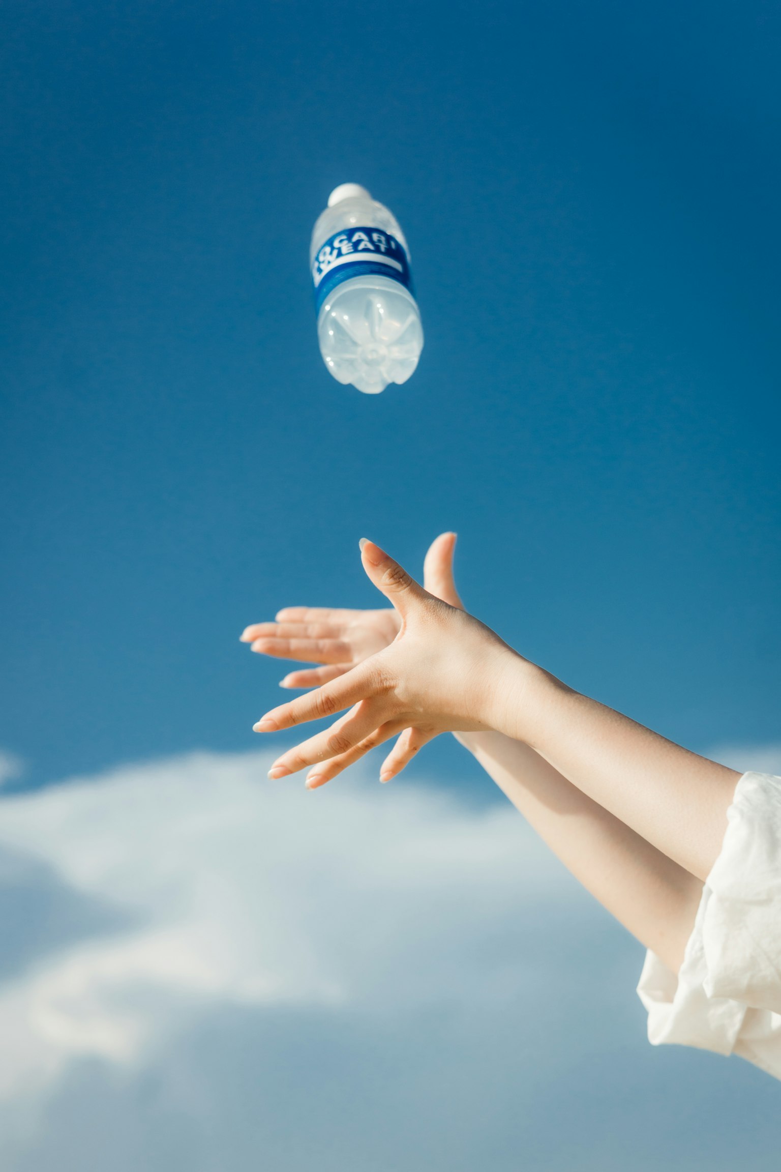 Una mano lanzando una botella de agua bajo un cielo azul