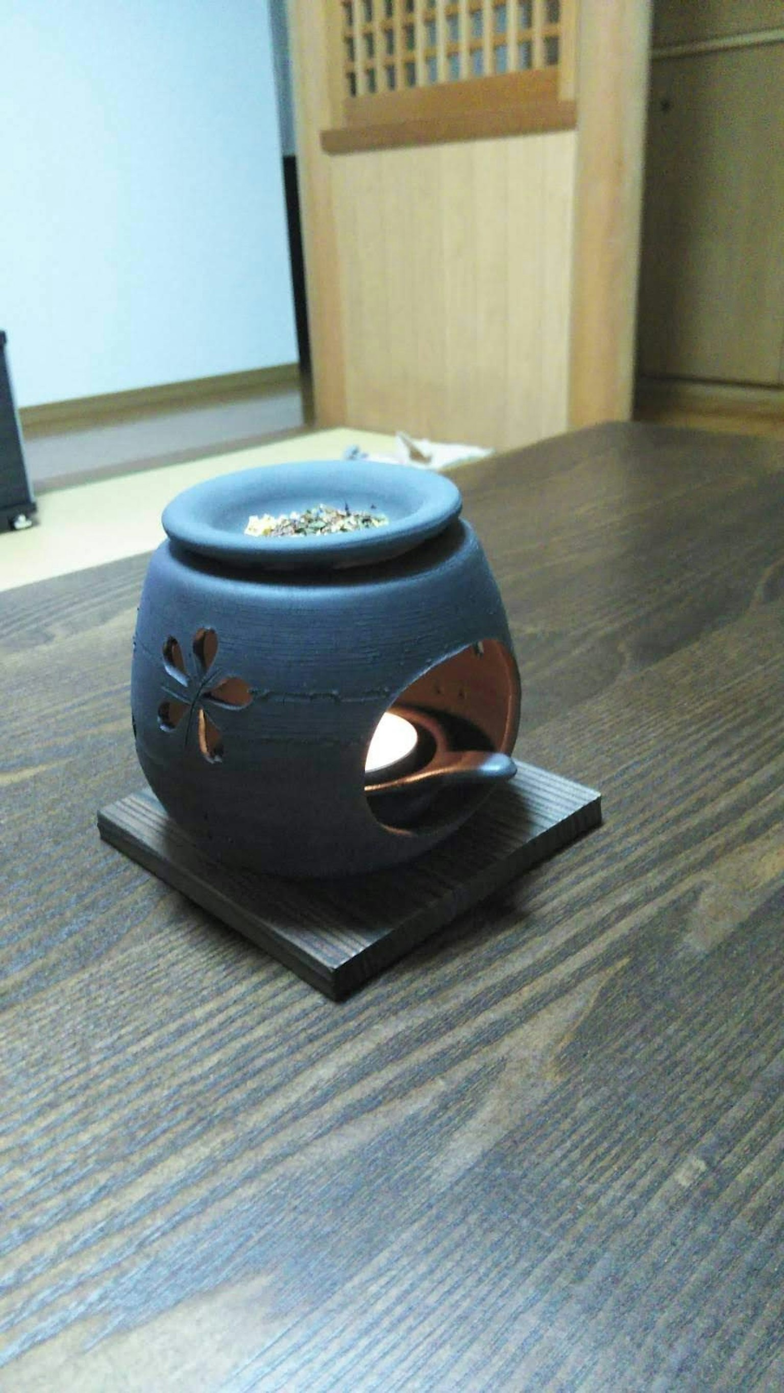 Sebuah pot aroma keramik hitam di atas meja kayu dengan lilin menyala di dalamnya