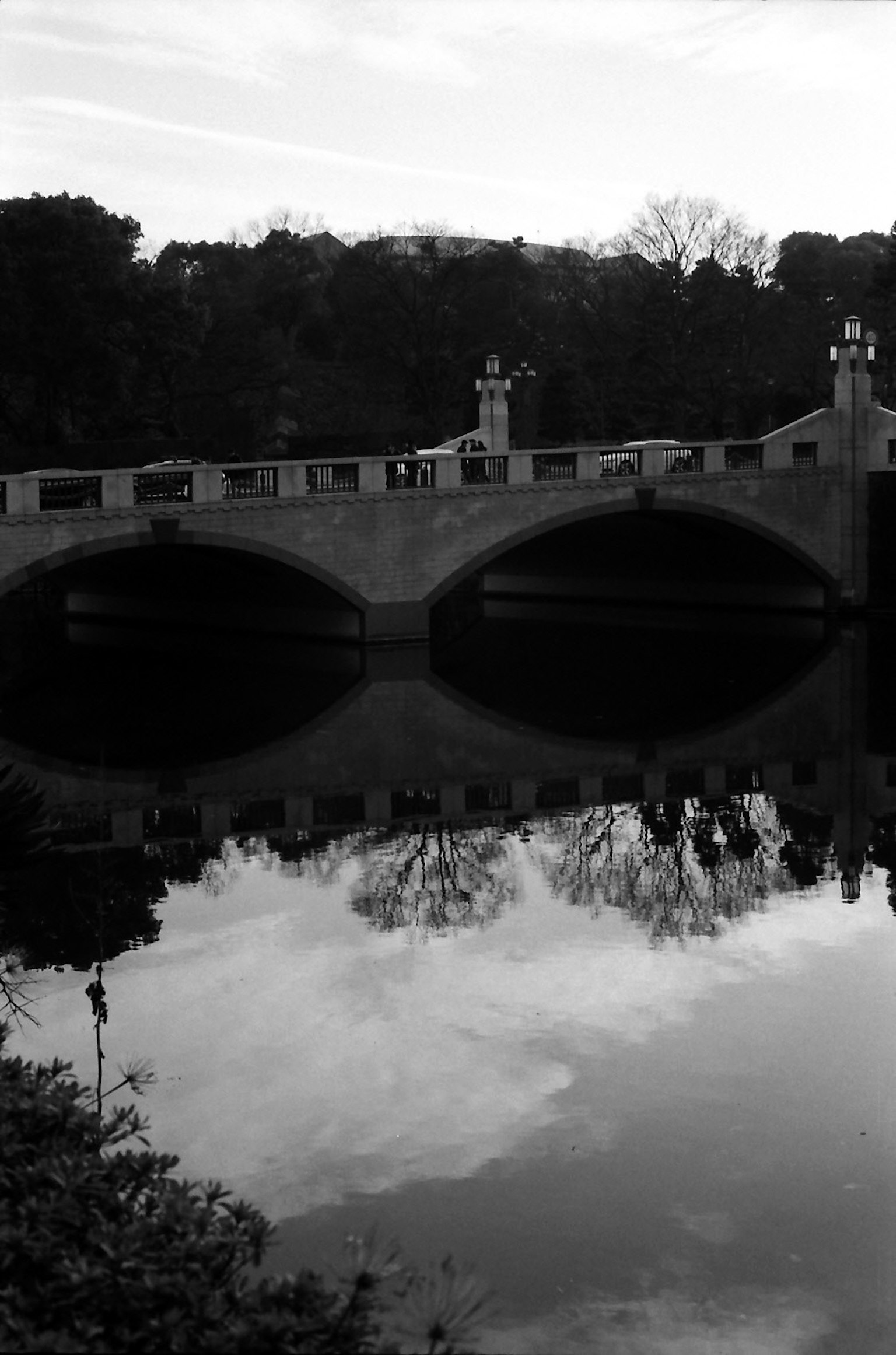 Black and white image of a bridge with reflections on still water