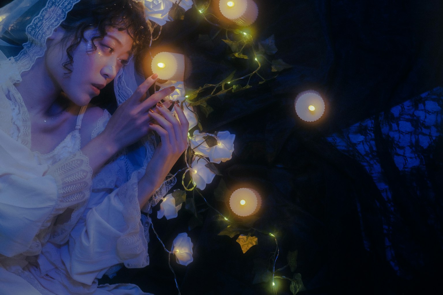 在深藍色背景中,穿著白色裙子的女性被白色花朵和發光燈飾圍繞