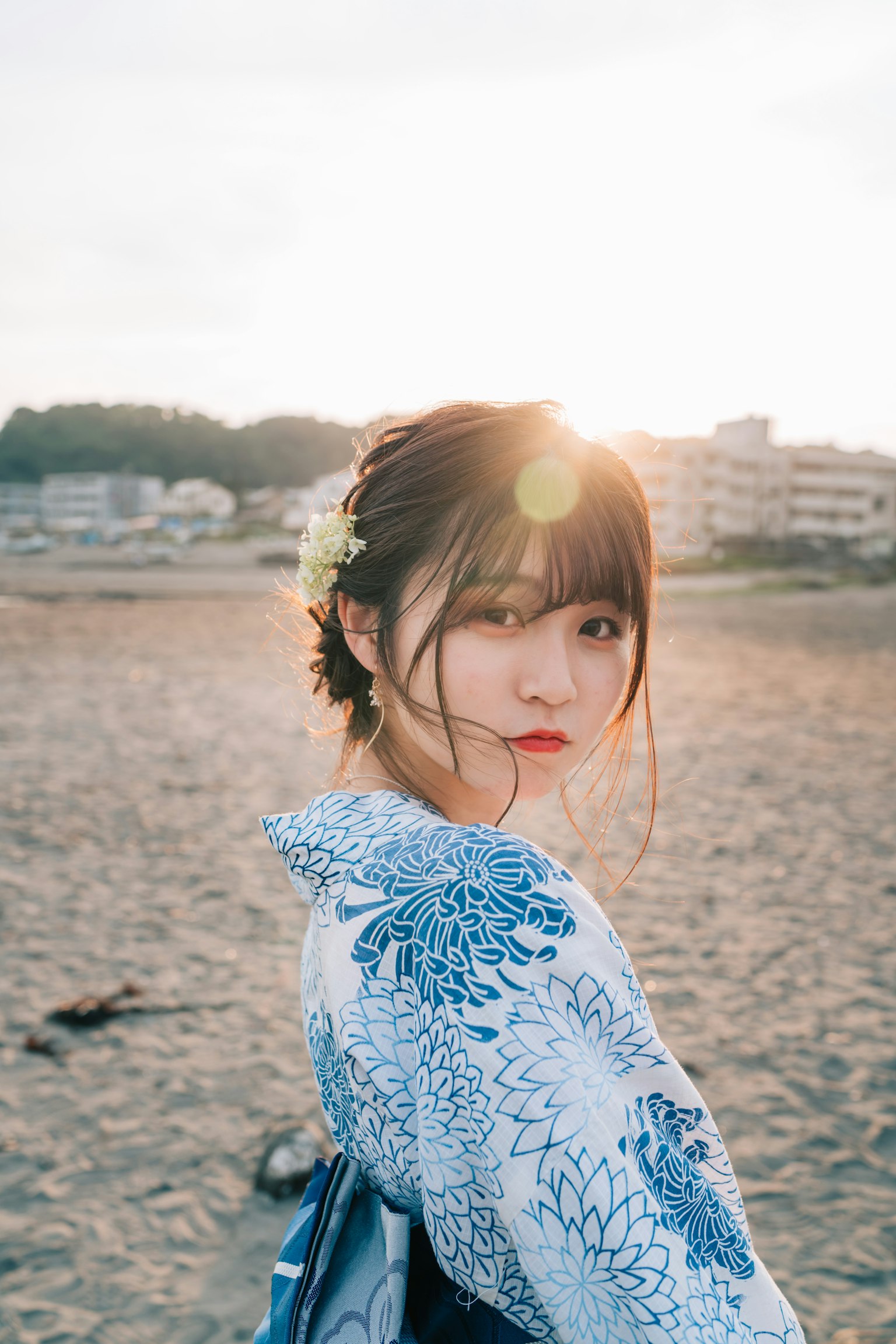 ภาพถ่ายหญิงสาวที่หันหลังกลับที่ชายหาด พร้อมด้วยเครื่องประดับดอกไม้และกิโมโนสีน้ำเงิน