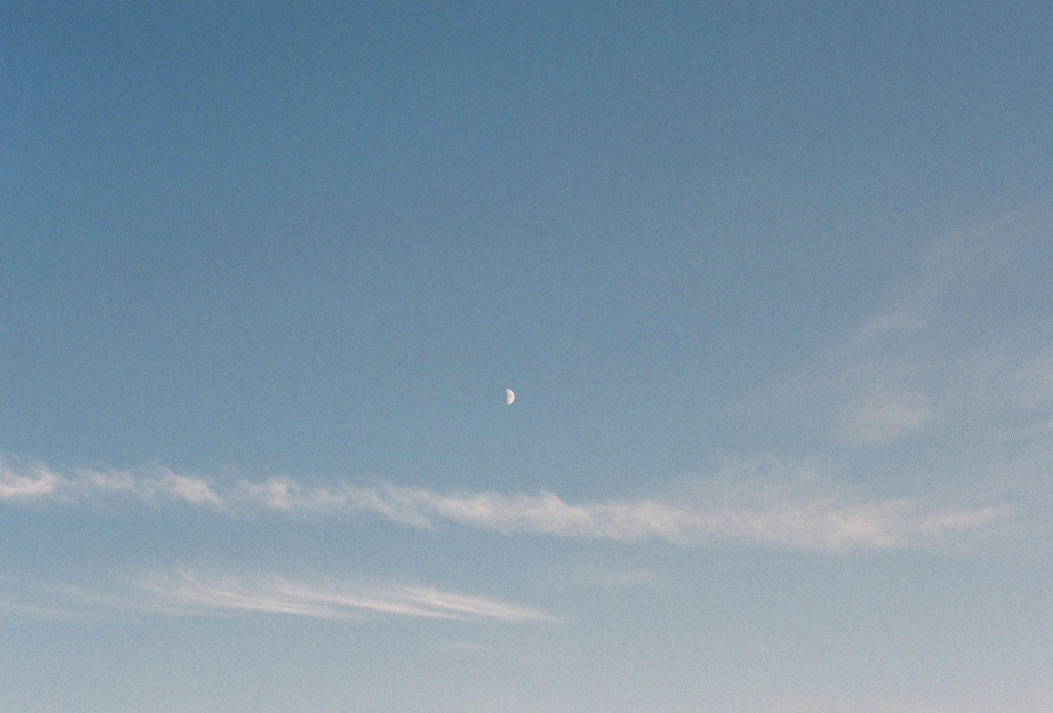 A clear blue sky with a crescent moon and wispy clouds