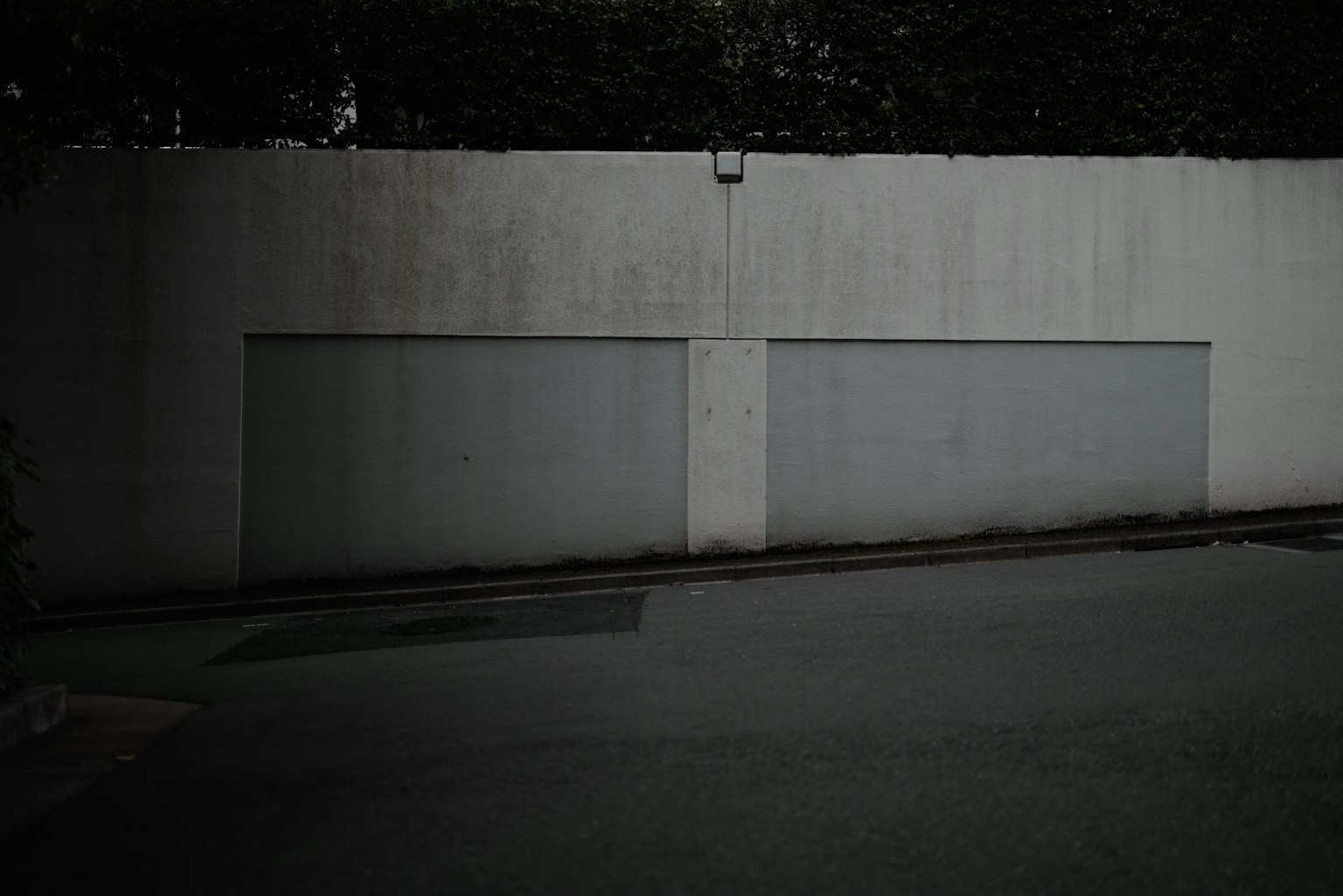 Betonwand mit zwei Garagentoren und gepflasterter Straße