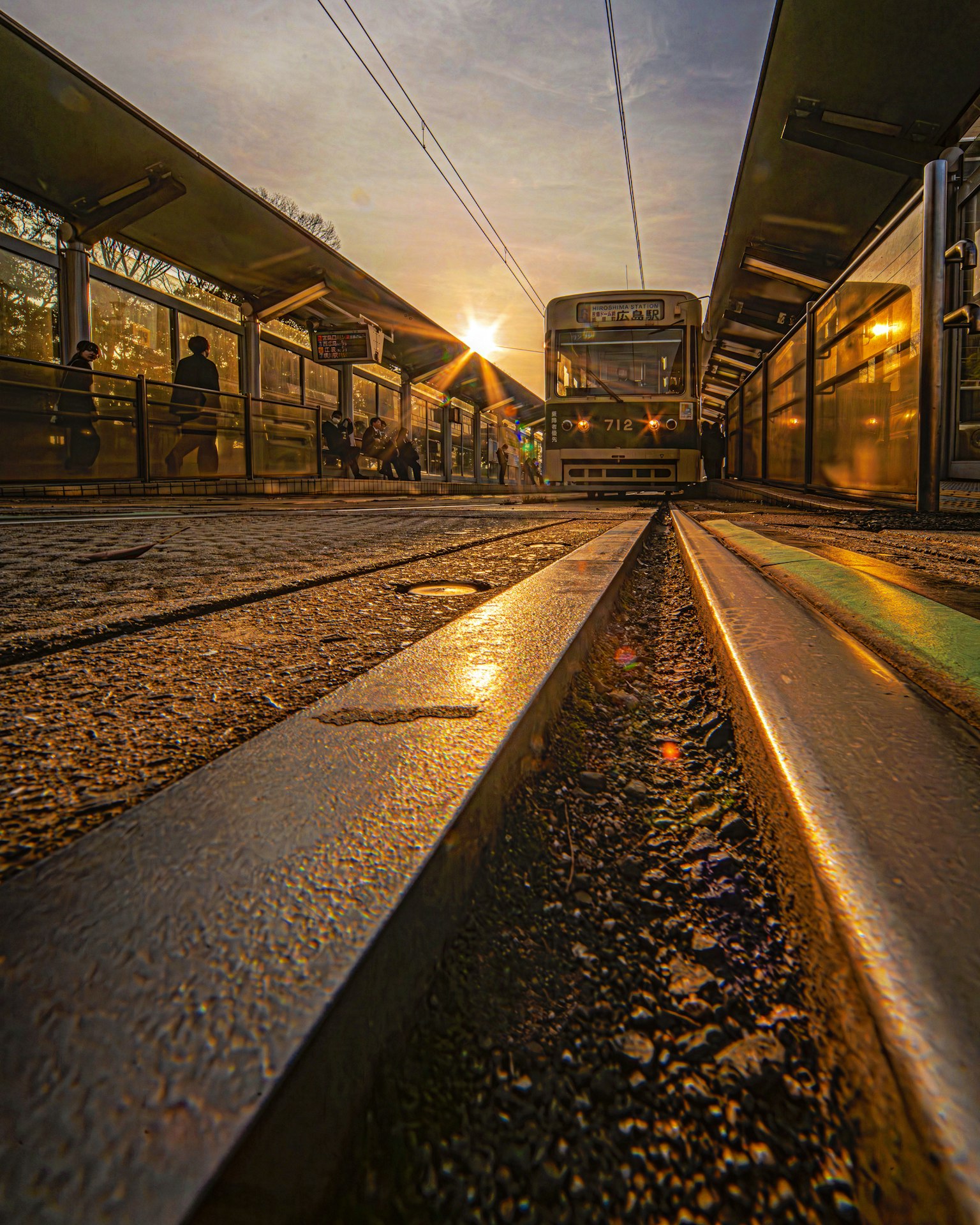 Tram stopped at a station with sunset lighting and railway perspective