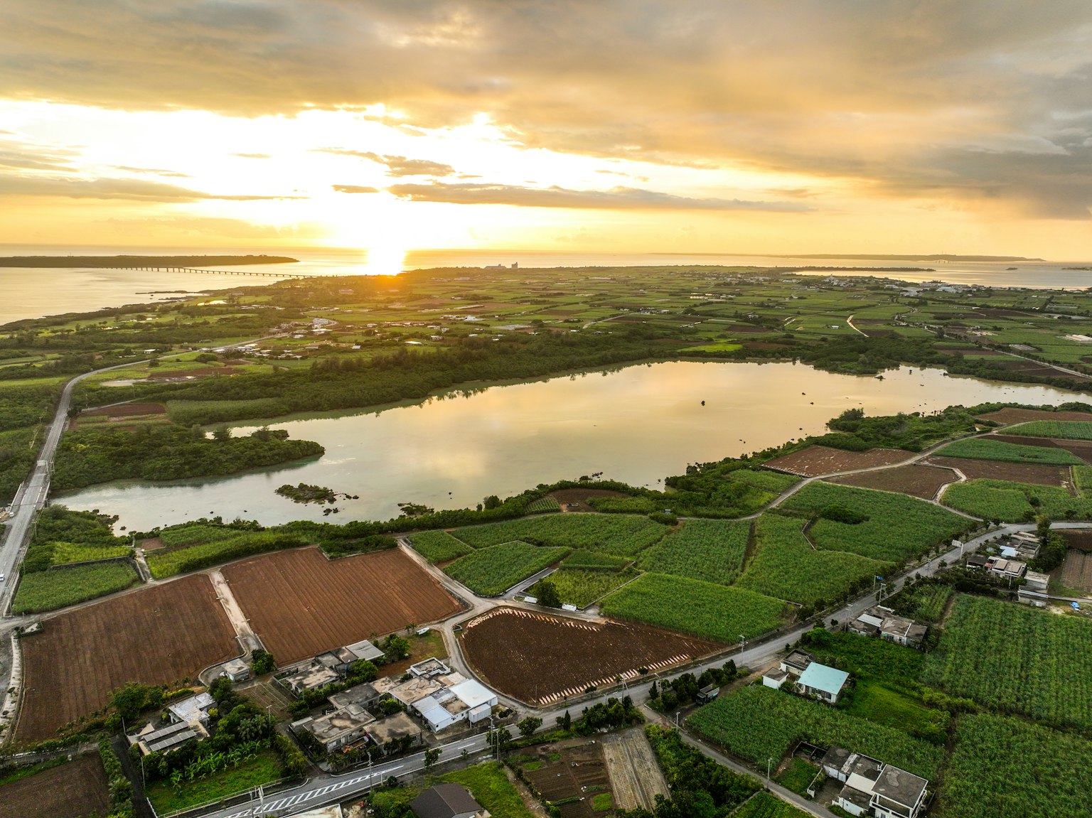 Scenic view of a sunset reflecting on a lake surrounded by lush farmland