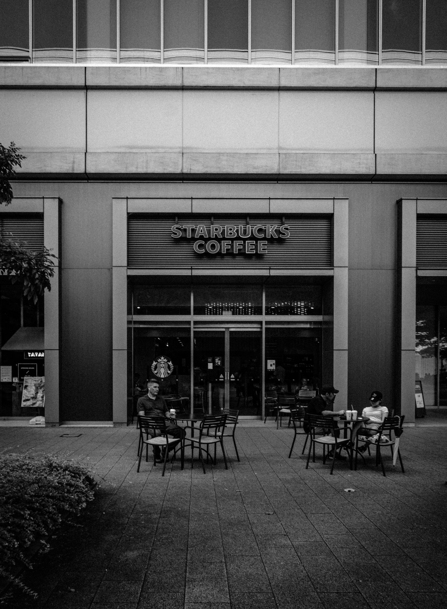 Schwarz-weiß-Foto eines Starbucks Coffee-Geschäfts mit Tischen und Stühlen im Freien