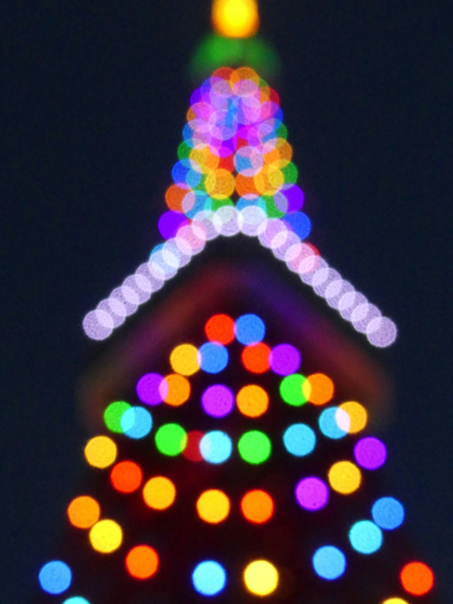 Bagian atas yang kabur dari pohon Natal dihiasi dengan lampu berwarna cerah