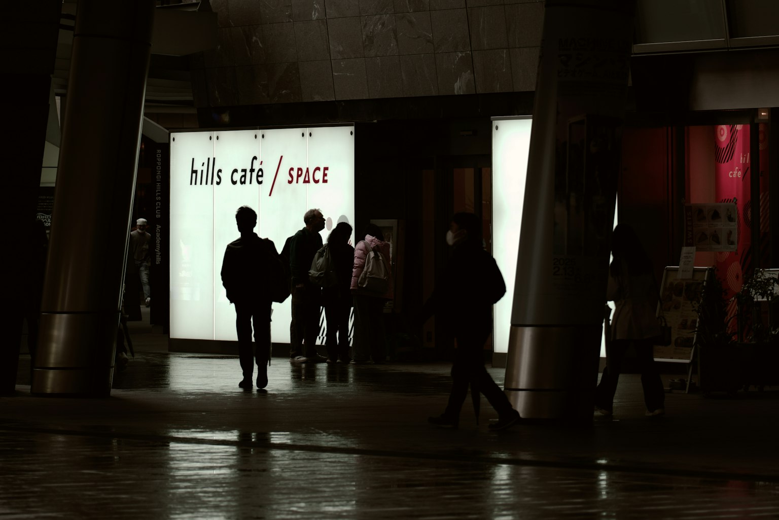 人々が「hills cafe / space」の看板の前に立っている夜の街の風景