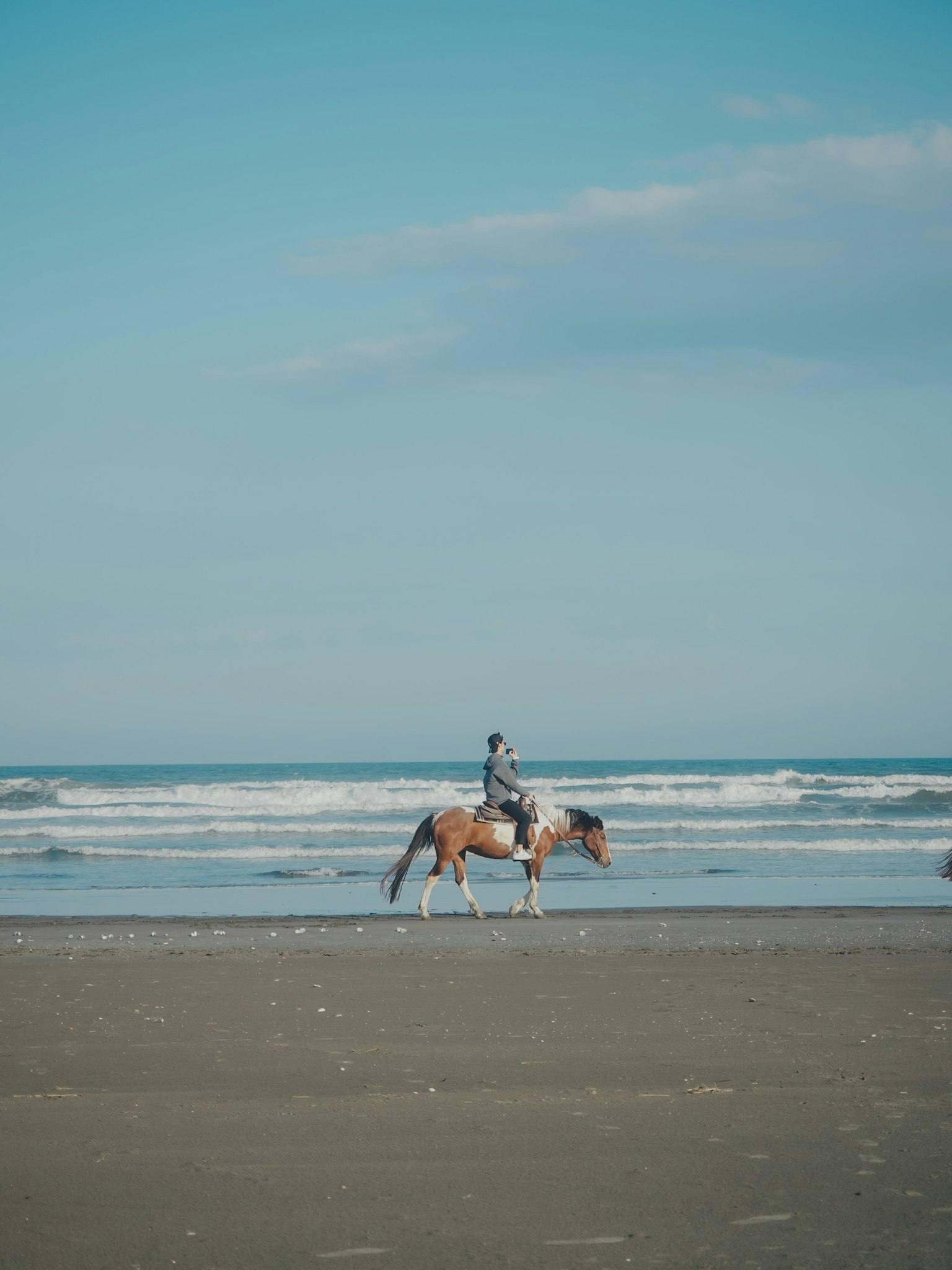 Un jinete en un caballo caminando por la playa con olas y cielo azul claro