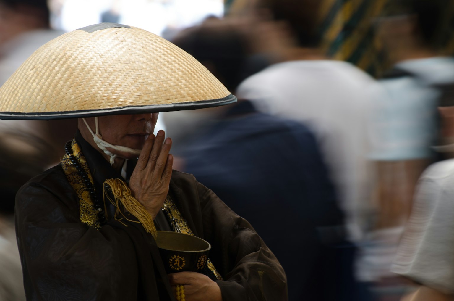 พระสงฆ์ที่สวมหมวกฟางและมือประนมอยู่ท่ามกลางฝูงชน