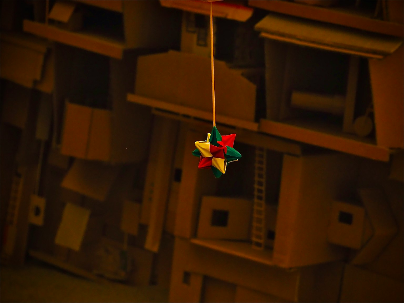 Objeto en forma de estrella colorida colgando frente a un fondo de estructuras de cartón