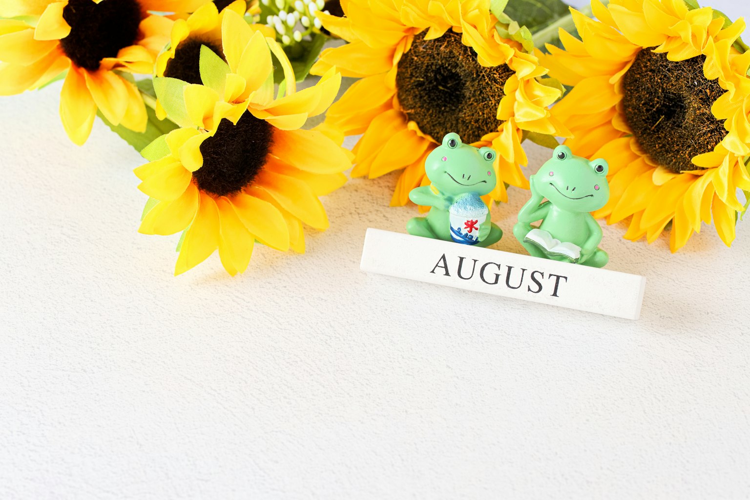 Froschfiguren, die August darstellen, neben einem Strauß Sonnenblumen