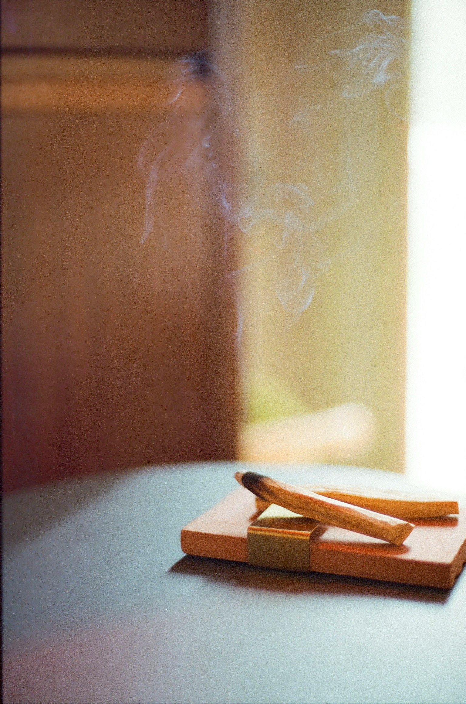 Incense sticks emitting smoke on a wooden holder in soft light