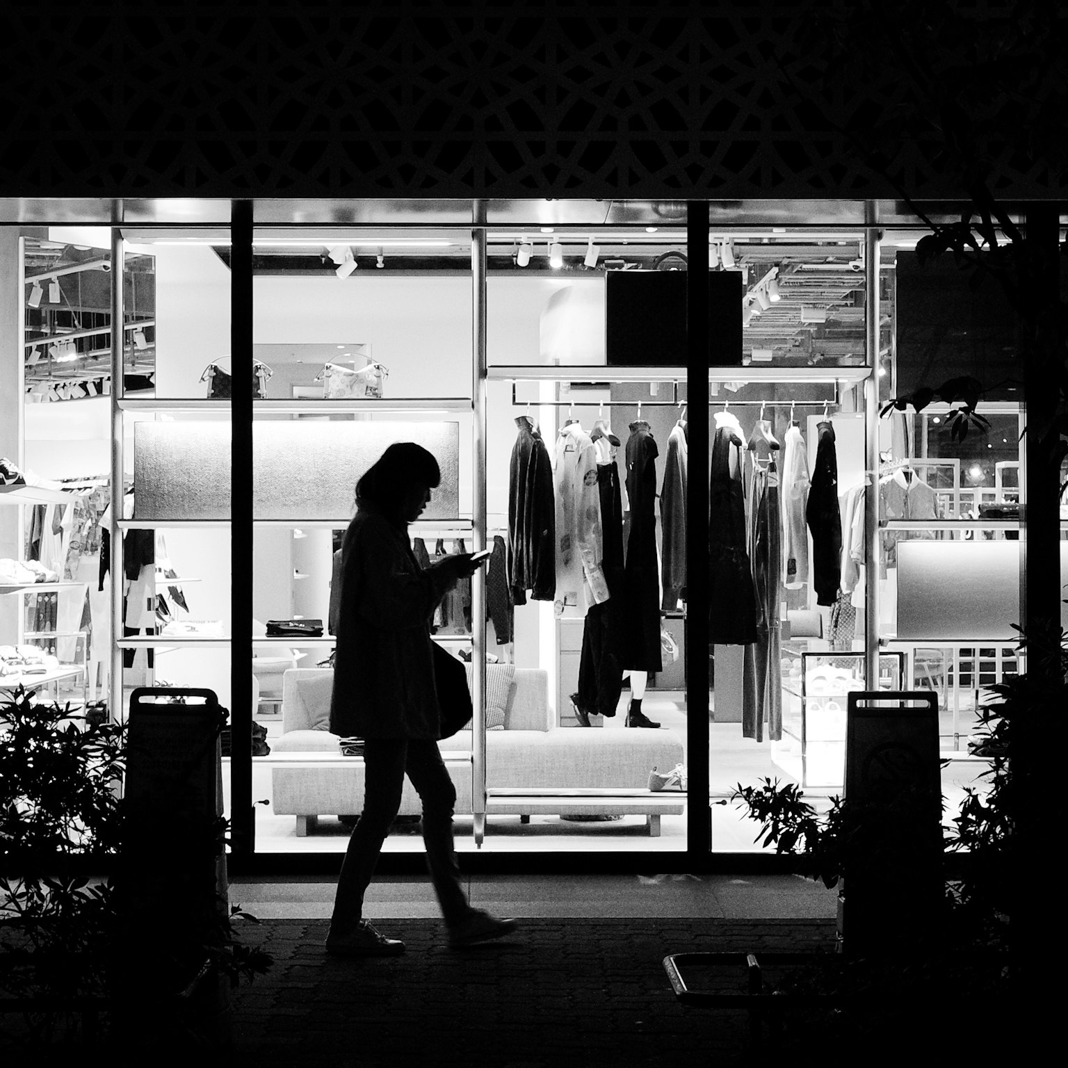 Silhouette of a woman walking past a store with clothing displayed inside