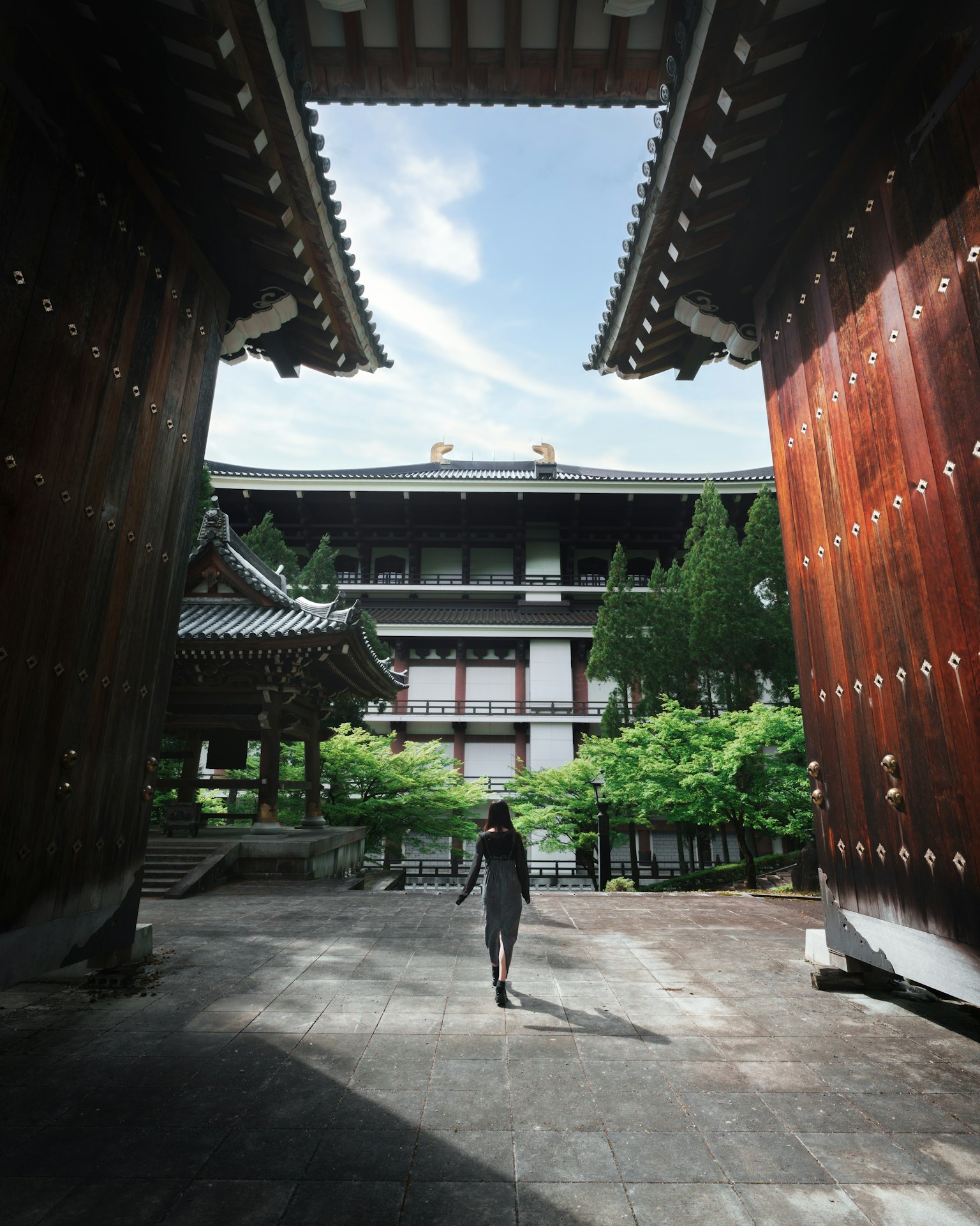 푸르른 배경 속에서 큰 나무 문을 지나가는 사람