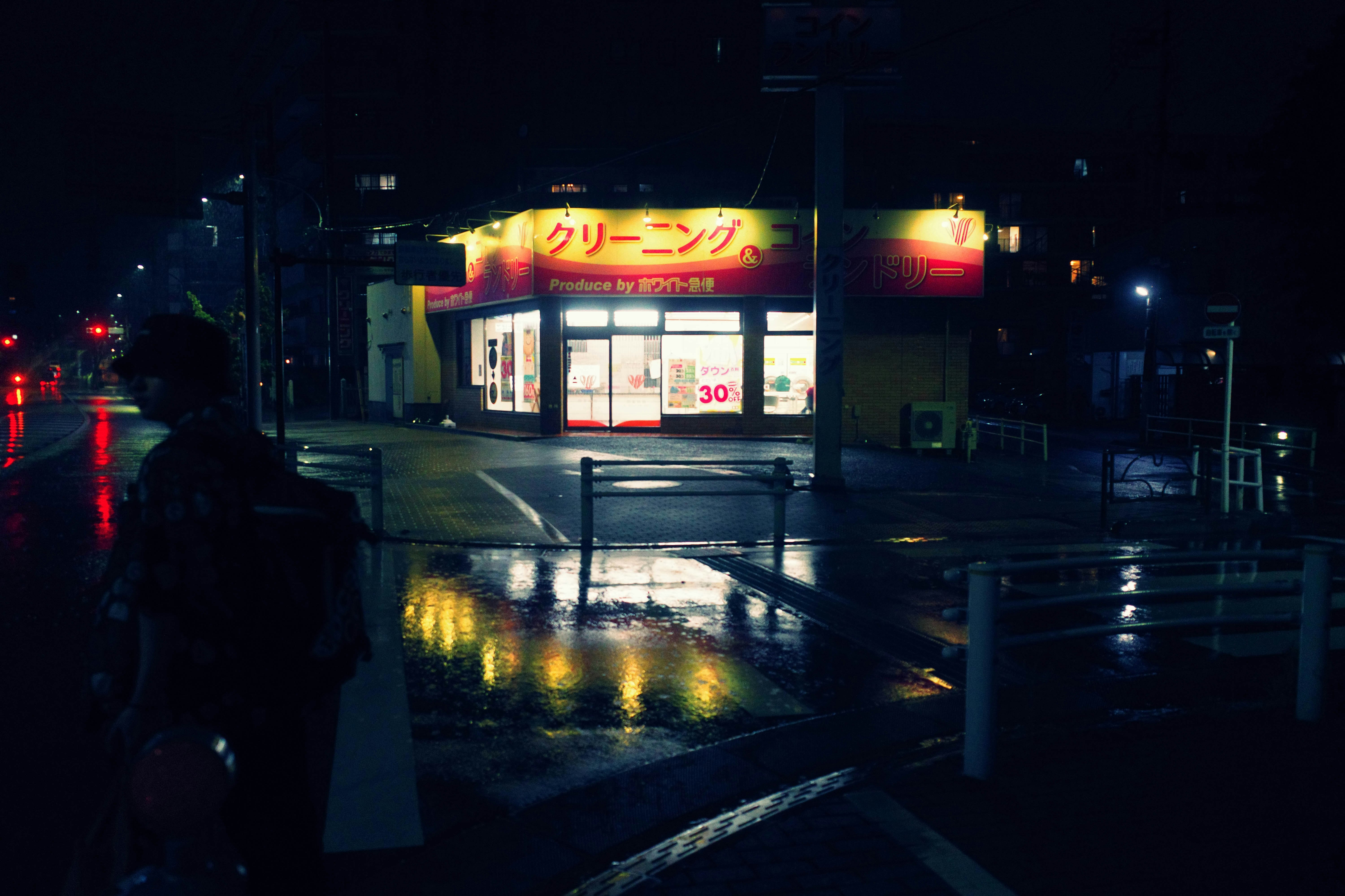 夜の雨上がりの街角にある看板と自販機のある店舗前