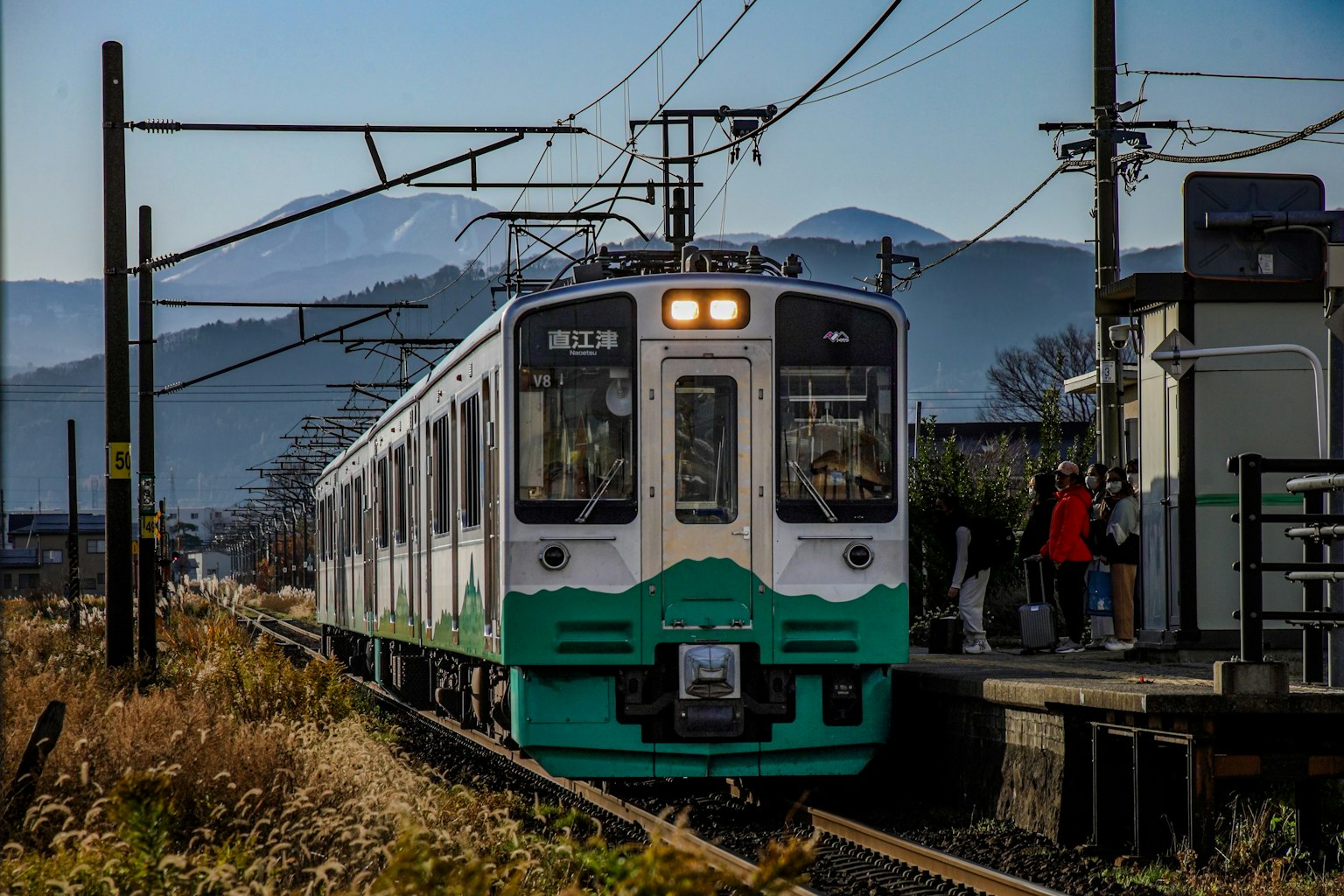 Un train vert et blanc s'arrêtant à une gare avec des montagnes en arrière-plan