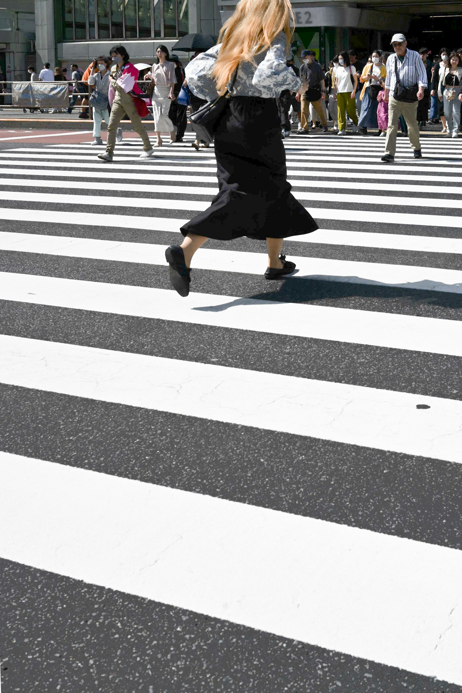 Blonde woman crossing a black and white crosswalk surrounded by people