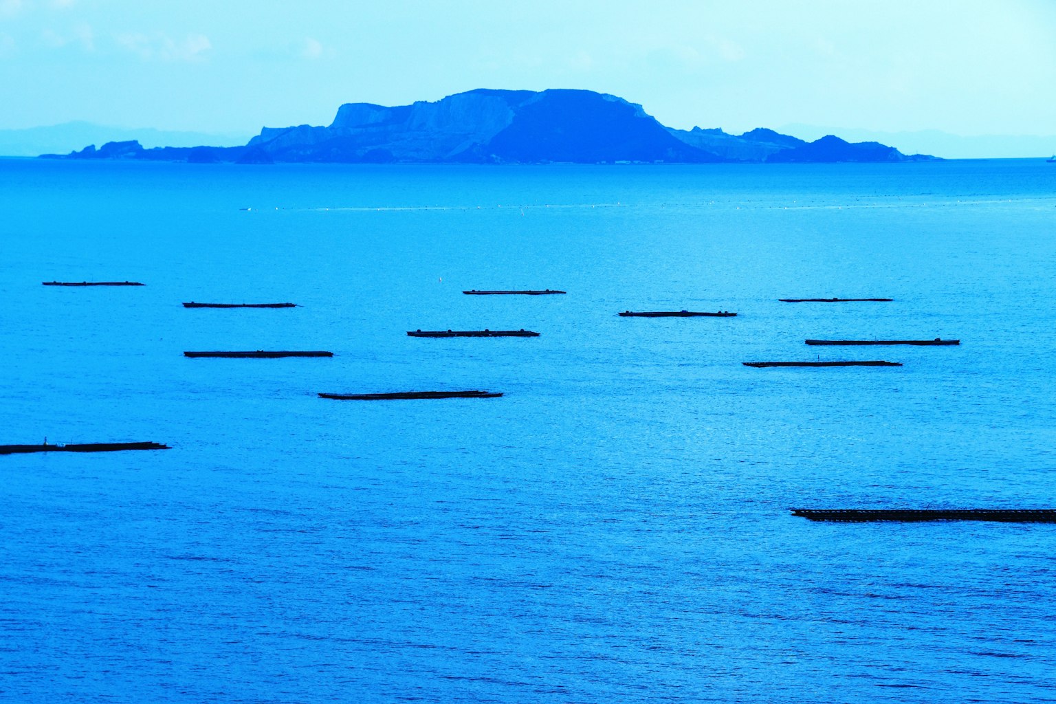 Blick auf ein blaues Meer mit einer fernen Insel und schwimmenden Fischereibooten