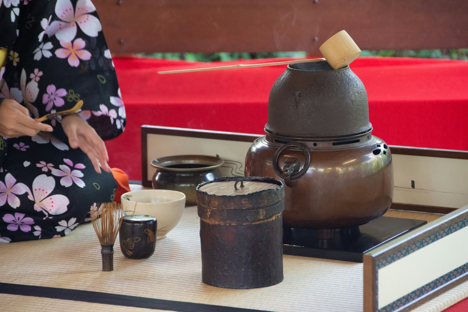 Una mujer en kimono preparando té con herramientas de ceremonia del té tradicionales