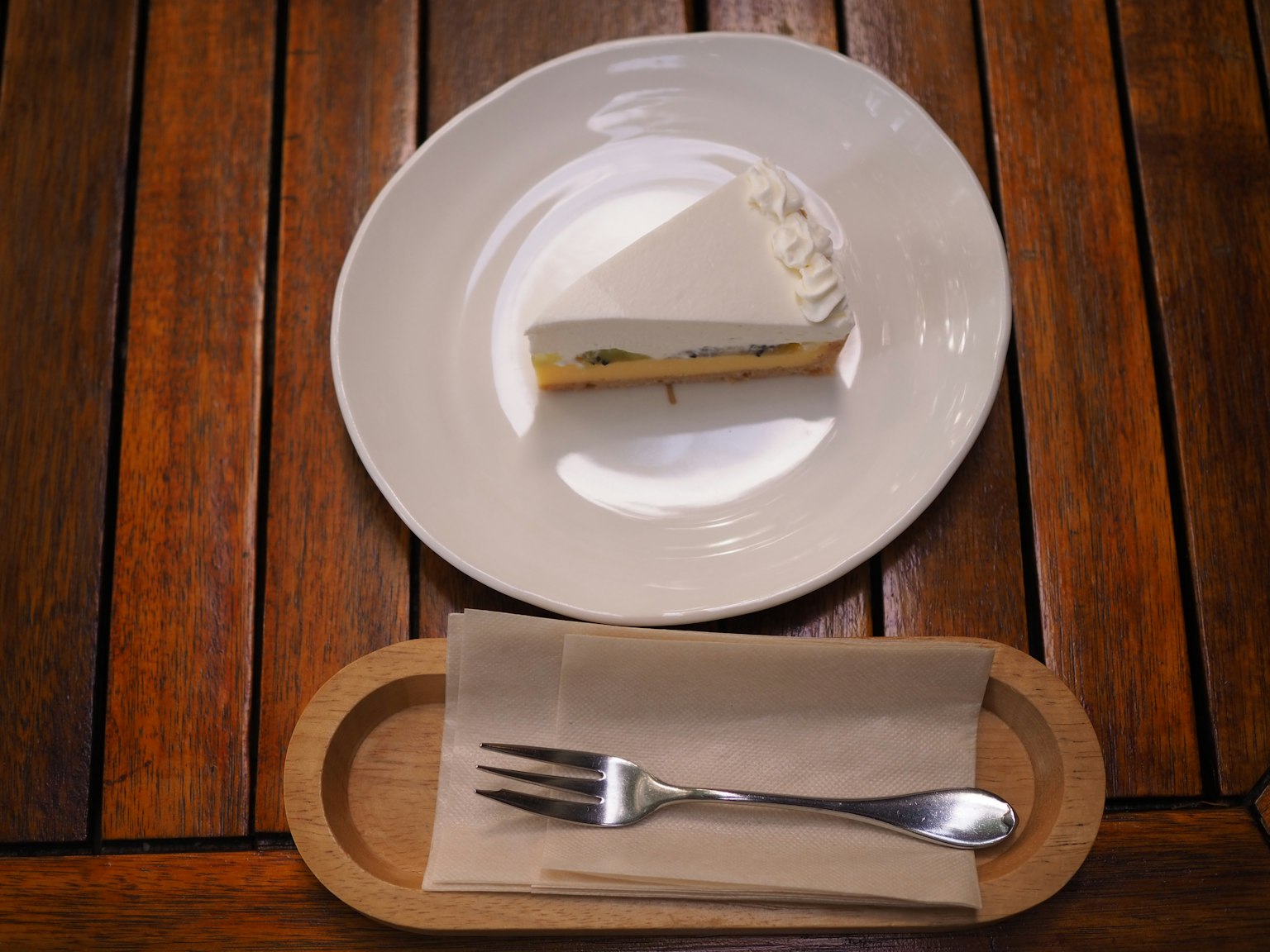 Una rebanada de pastel blanco en un plato blanco sobre una mesa de madera