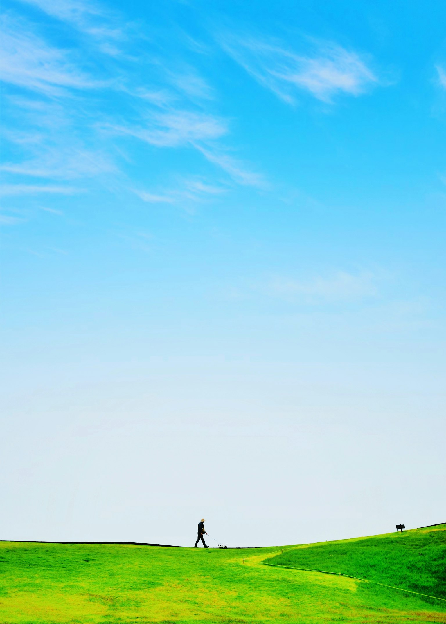 A person walking on green hills under a blue sky