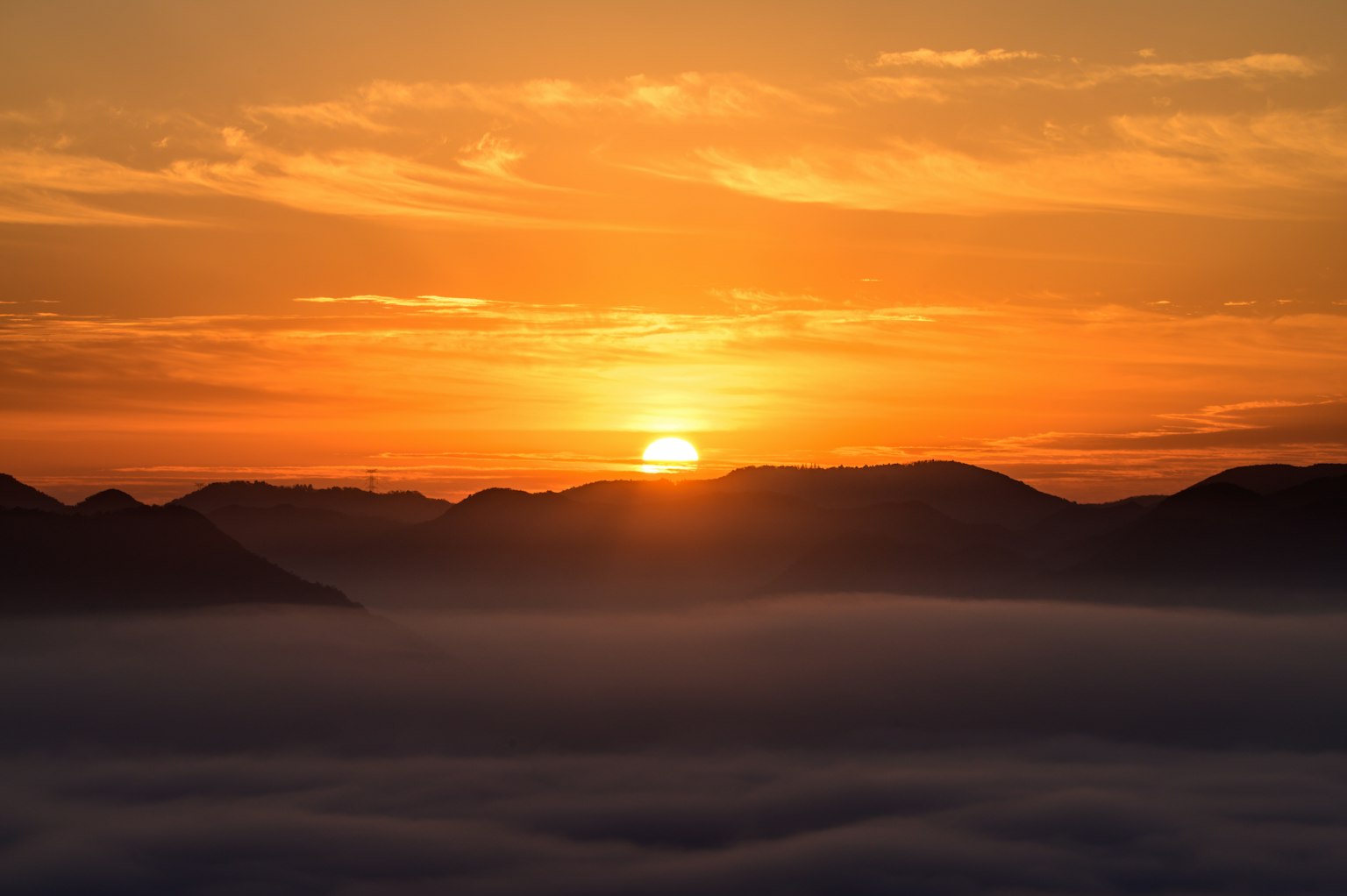 Orange sun rising over mountains with a sea of clouds