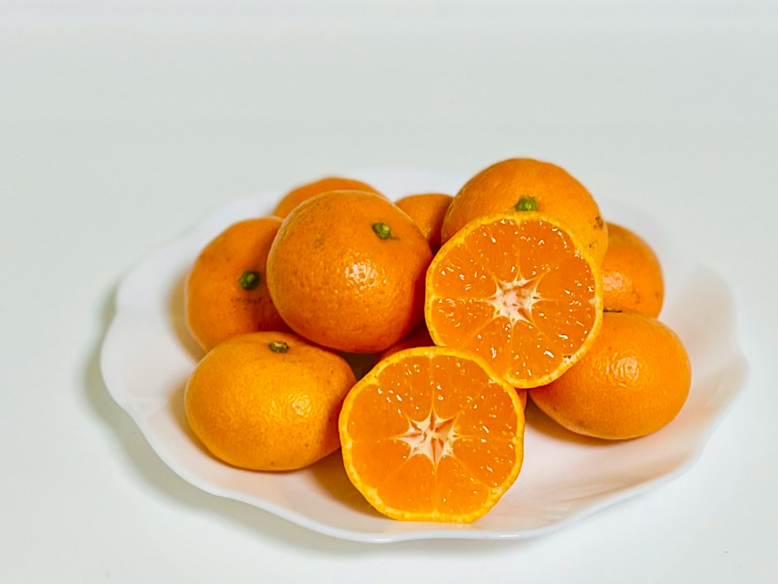 A pile of oranges on a white plate with a halved orange