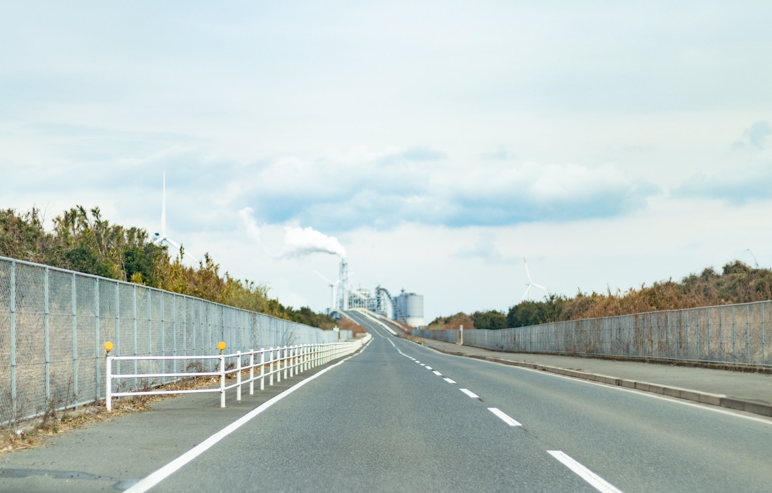 Breite Straße mit sichtbaren Fabrikschornsteinen im Hintergrund