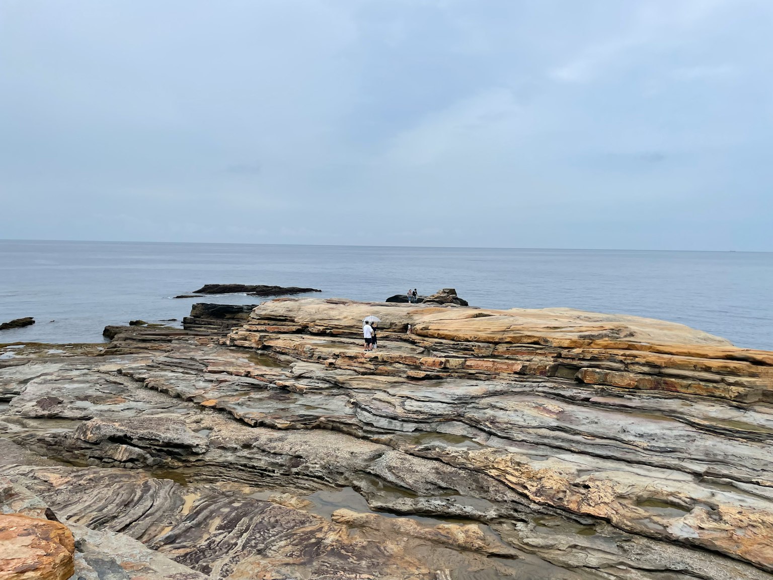 Eine Person steht auf felsigem Gelände am ruhigen Meer