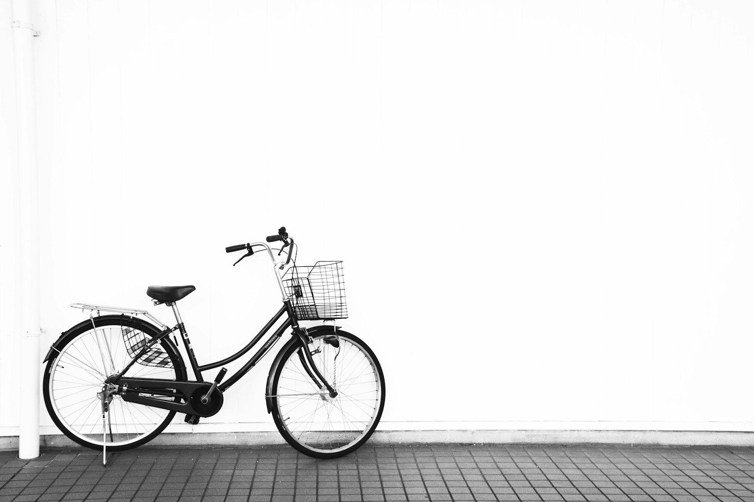 Bicicletta nera con cestino appoggiata a un muro bianco